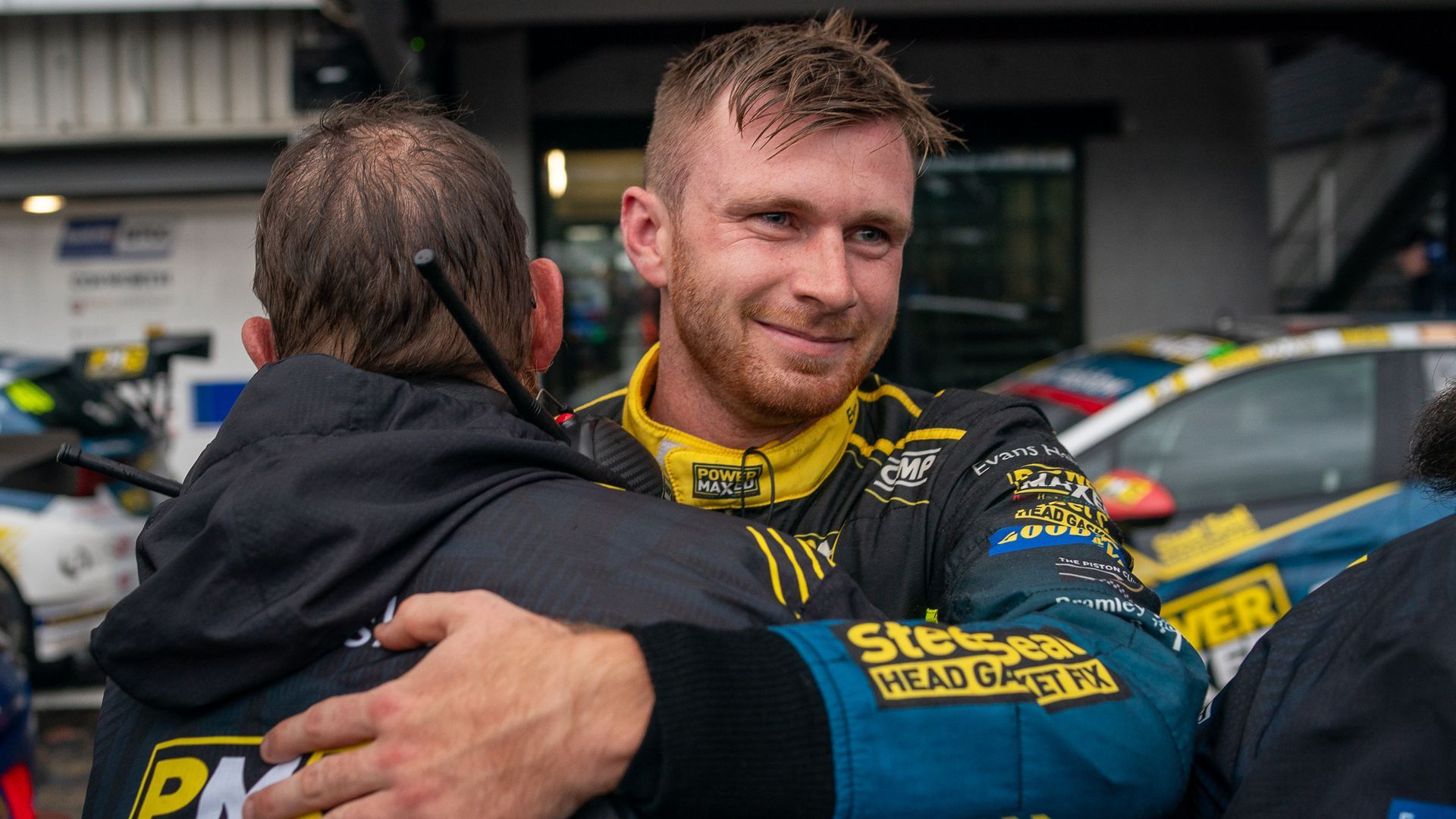 A man is hugging another man in front of a race car.