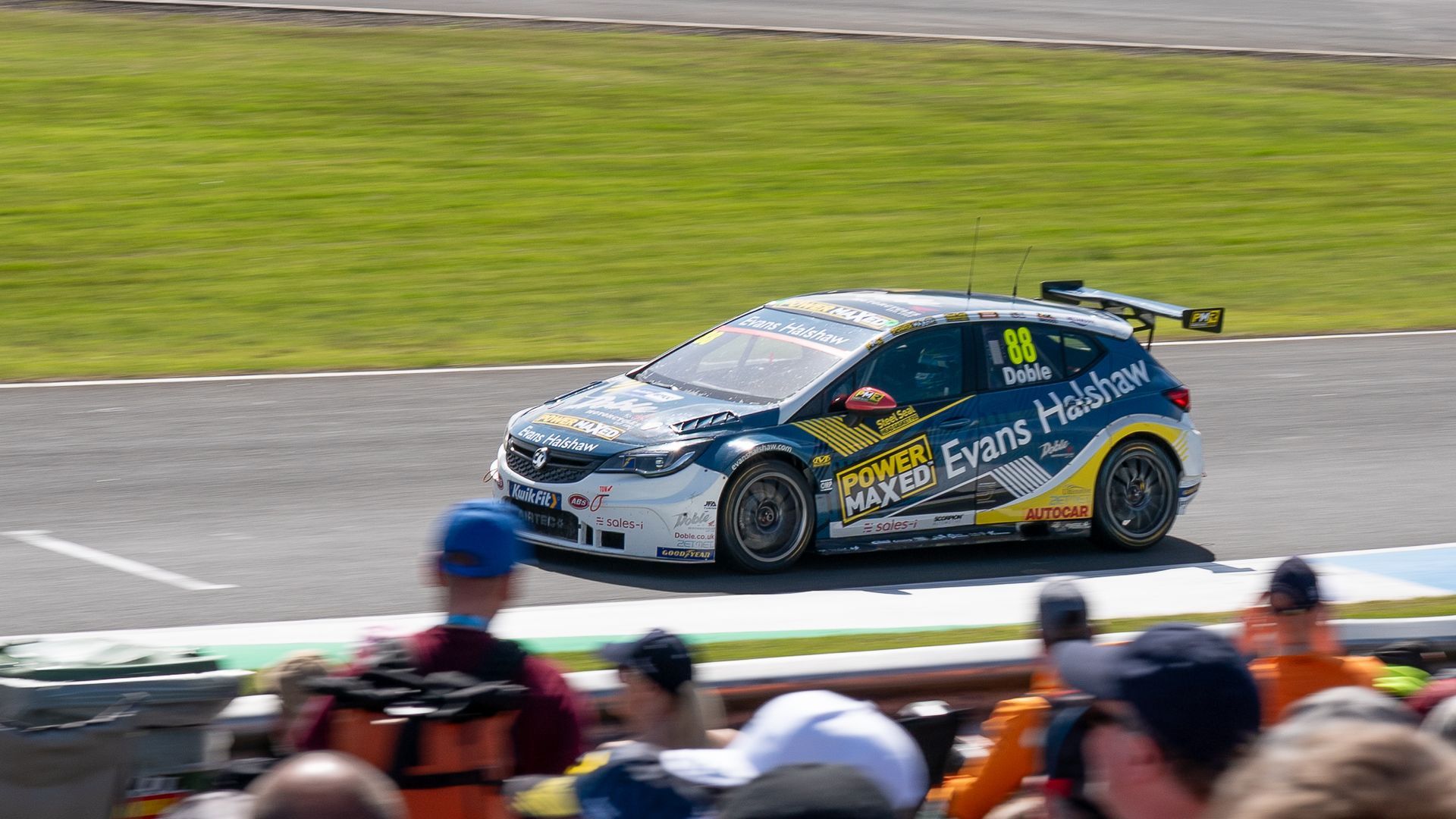 A race car is driving down a track with a crowd watching.