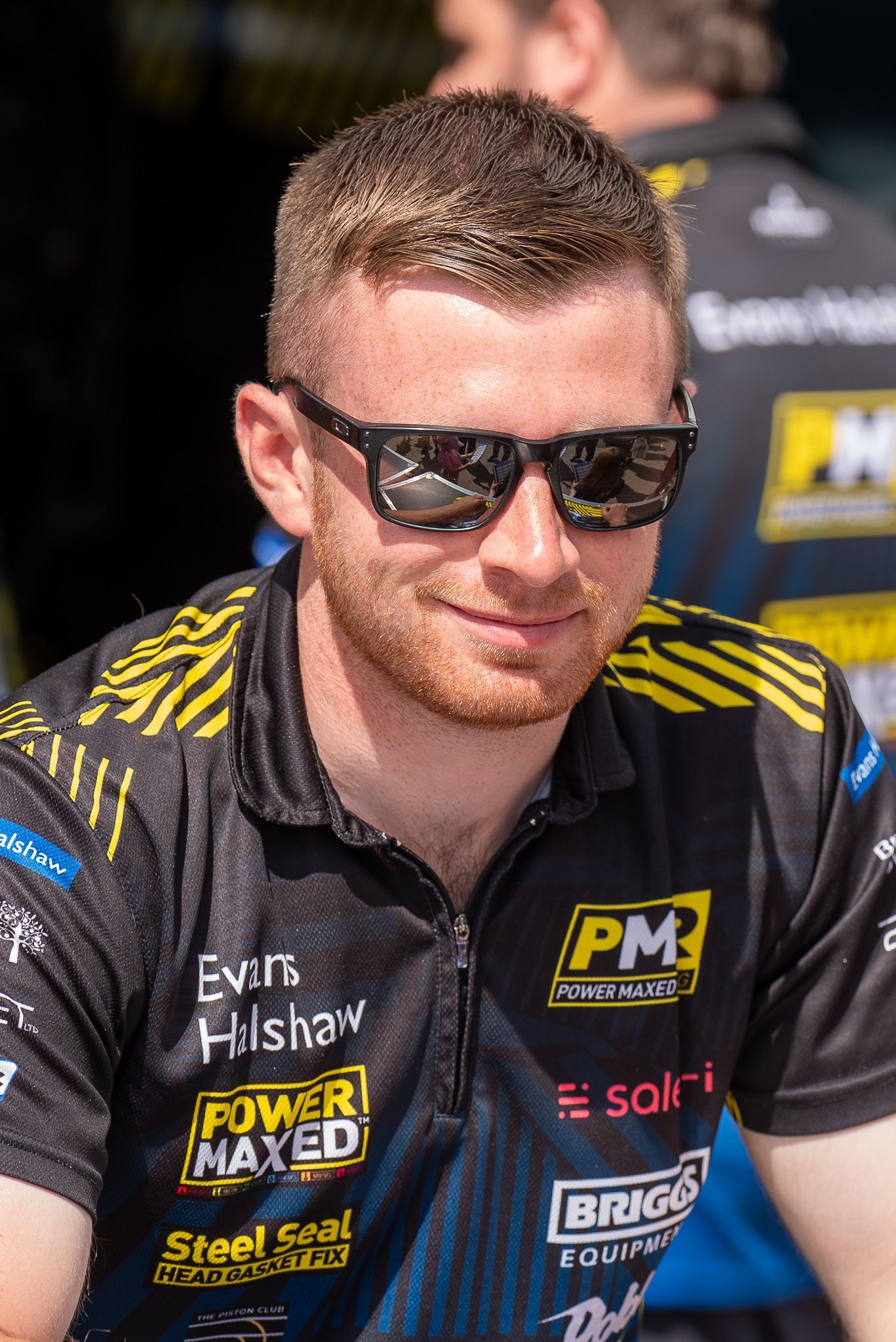 A man wearing sunglasses and a black shirt with logos on it.