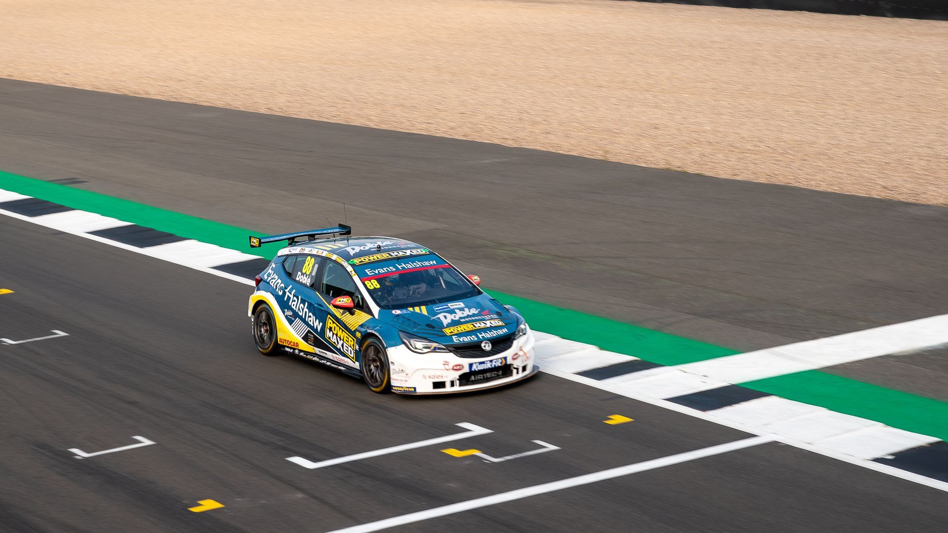 A blue and yellow race car is driving down a race track.