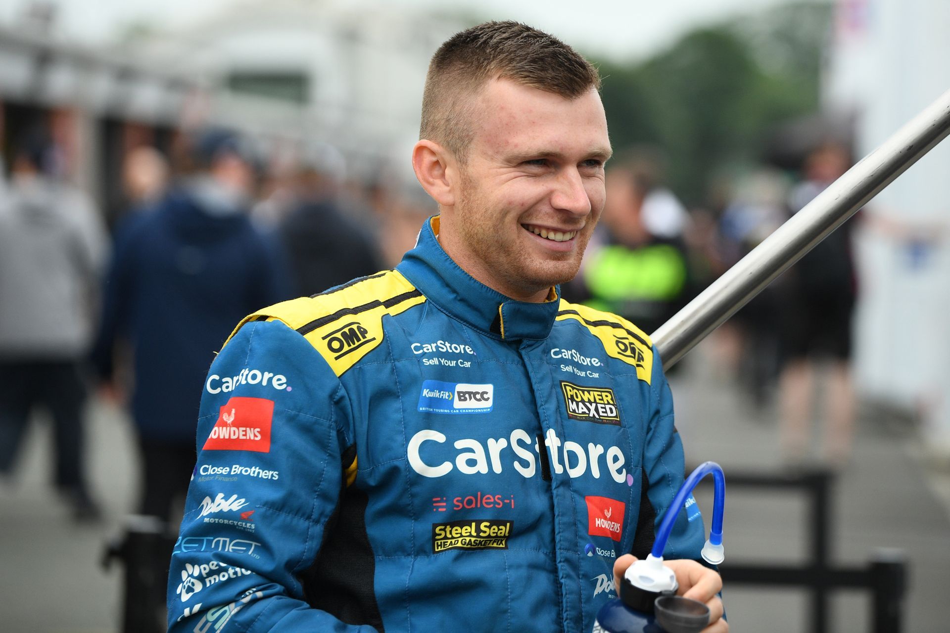 A man in a blue and yellow racing suit is holding an umbrella.