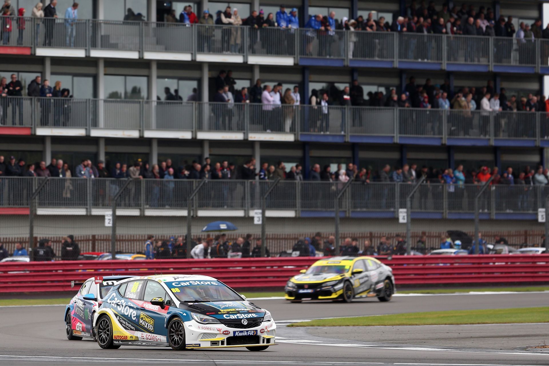 A group of cars are racing on a race track in front of a crowd.