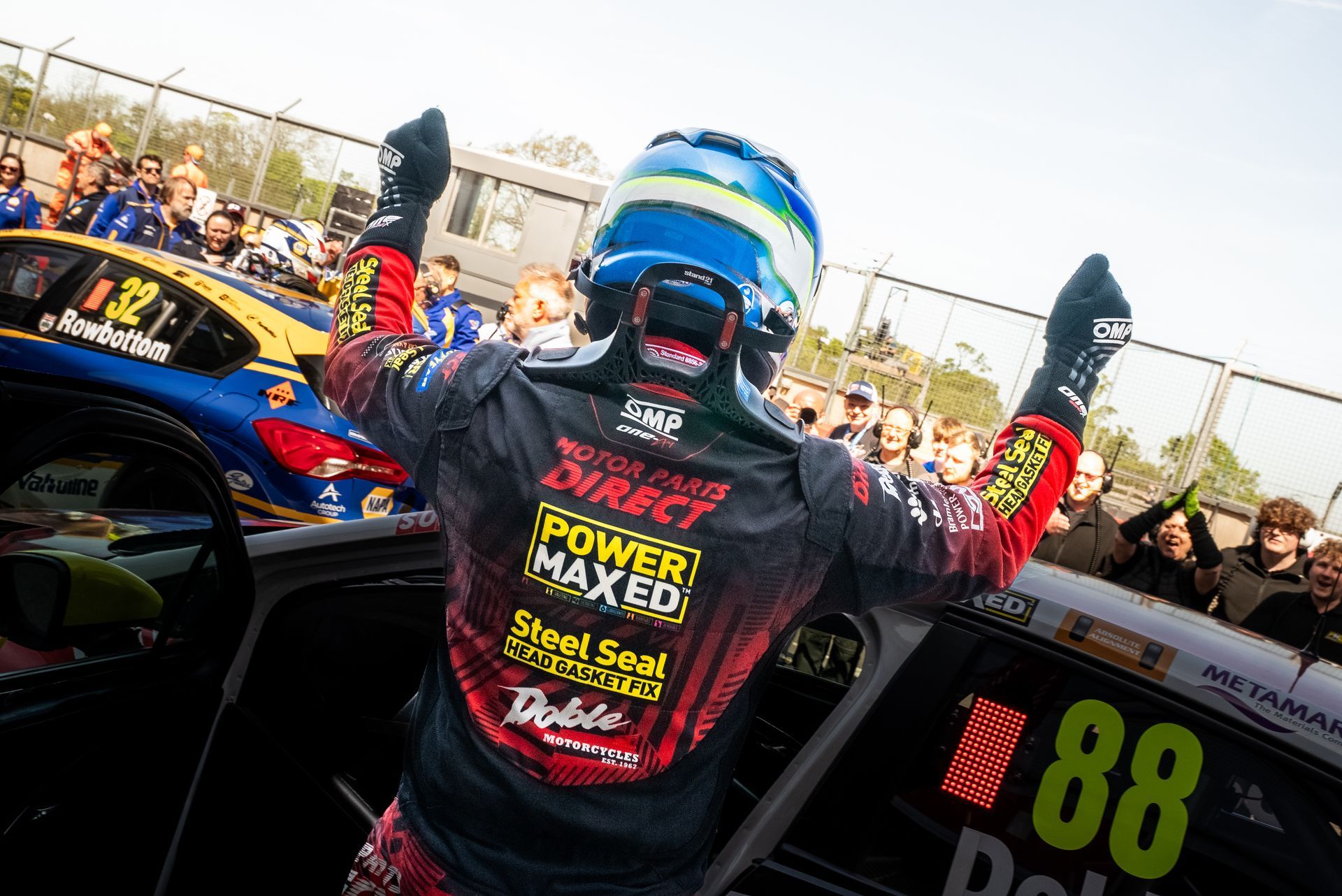 A man is standing in front of a race car with his arms in the air.