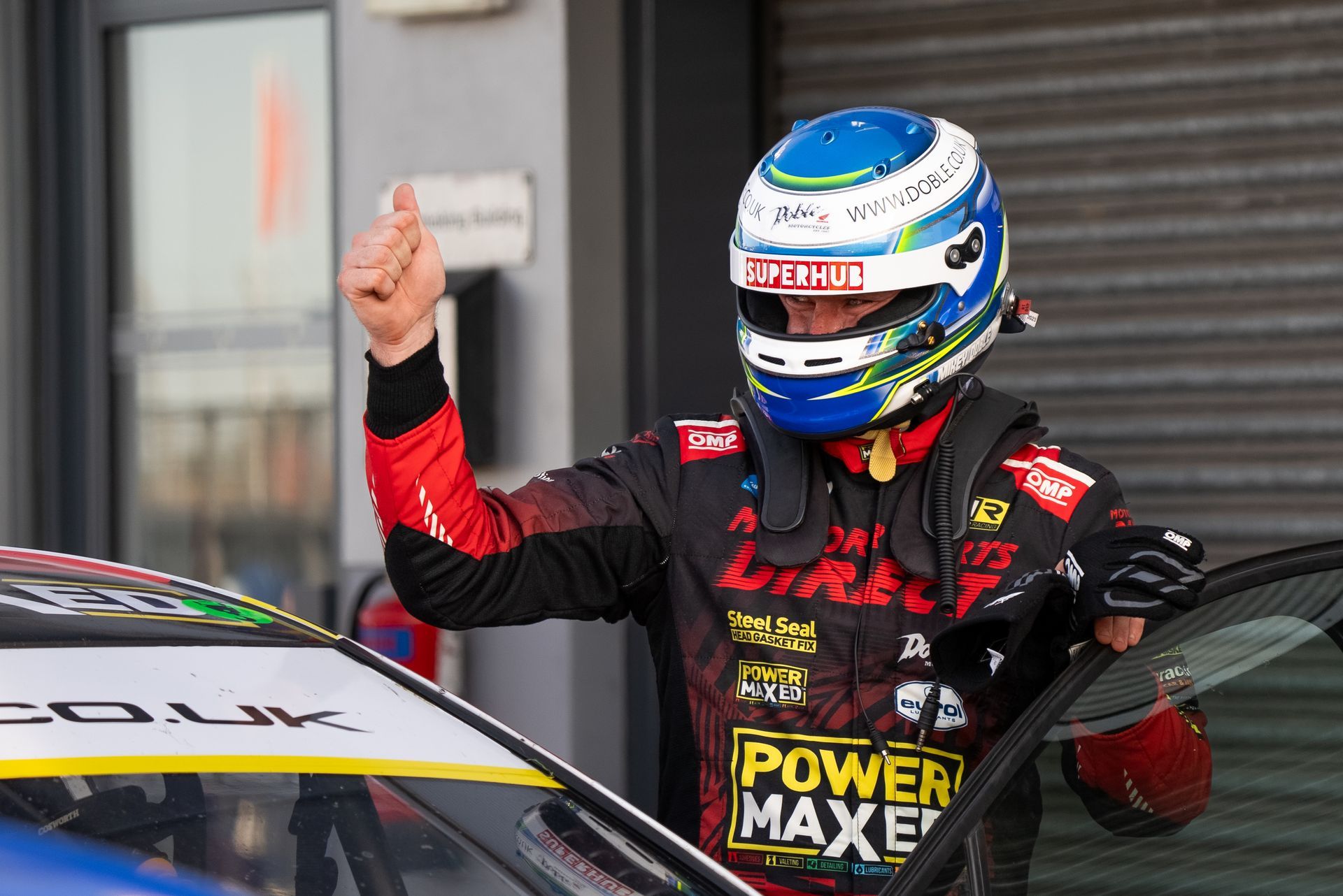 A man wearing a helmet is standing next to a race car.