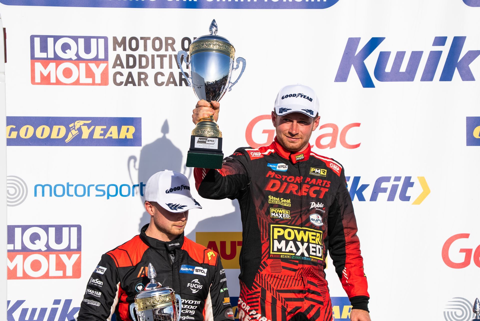 Two men are standing on a podium holding a trophy.