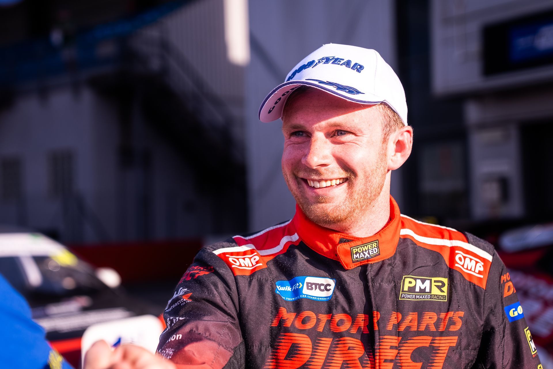 A man in a racing suit and hat is shaking hands with another man.