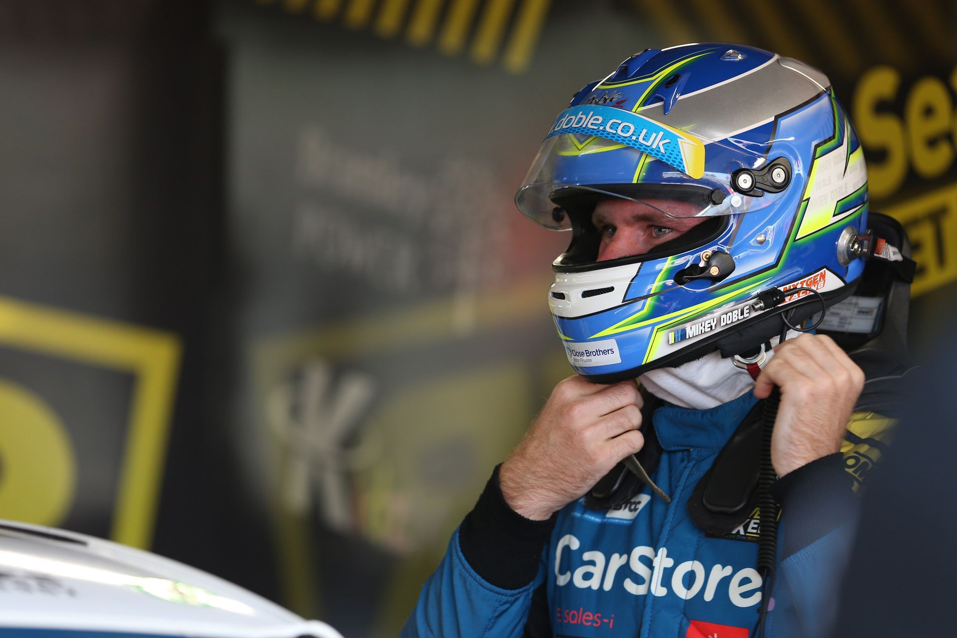 A man wearing a helmet and a carstore shirt is putting on his helmet.
