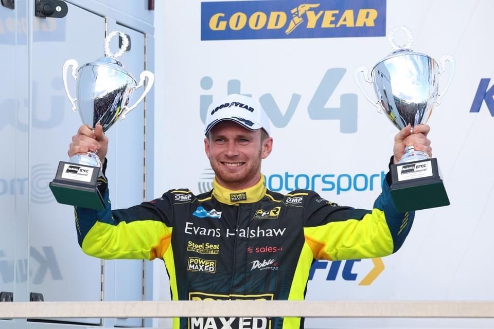 A man is holding two trophies in front of a good year sign
