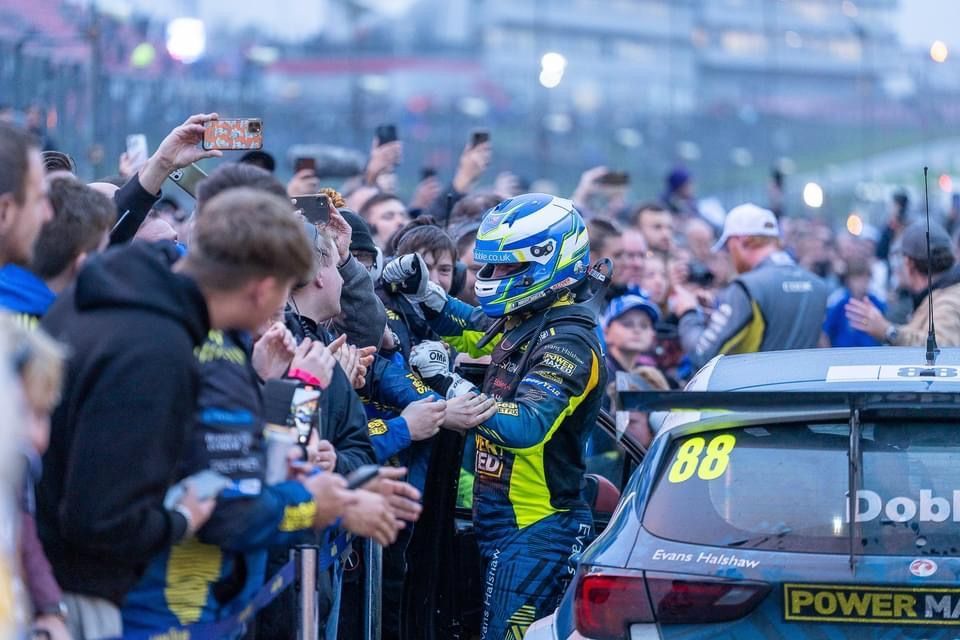 A man in a helmet is standing next to a race car in front of a crowd of people.
