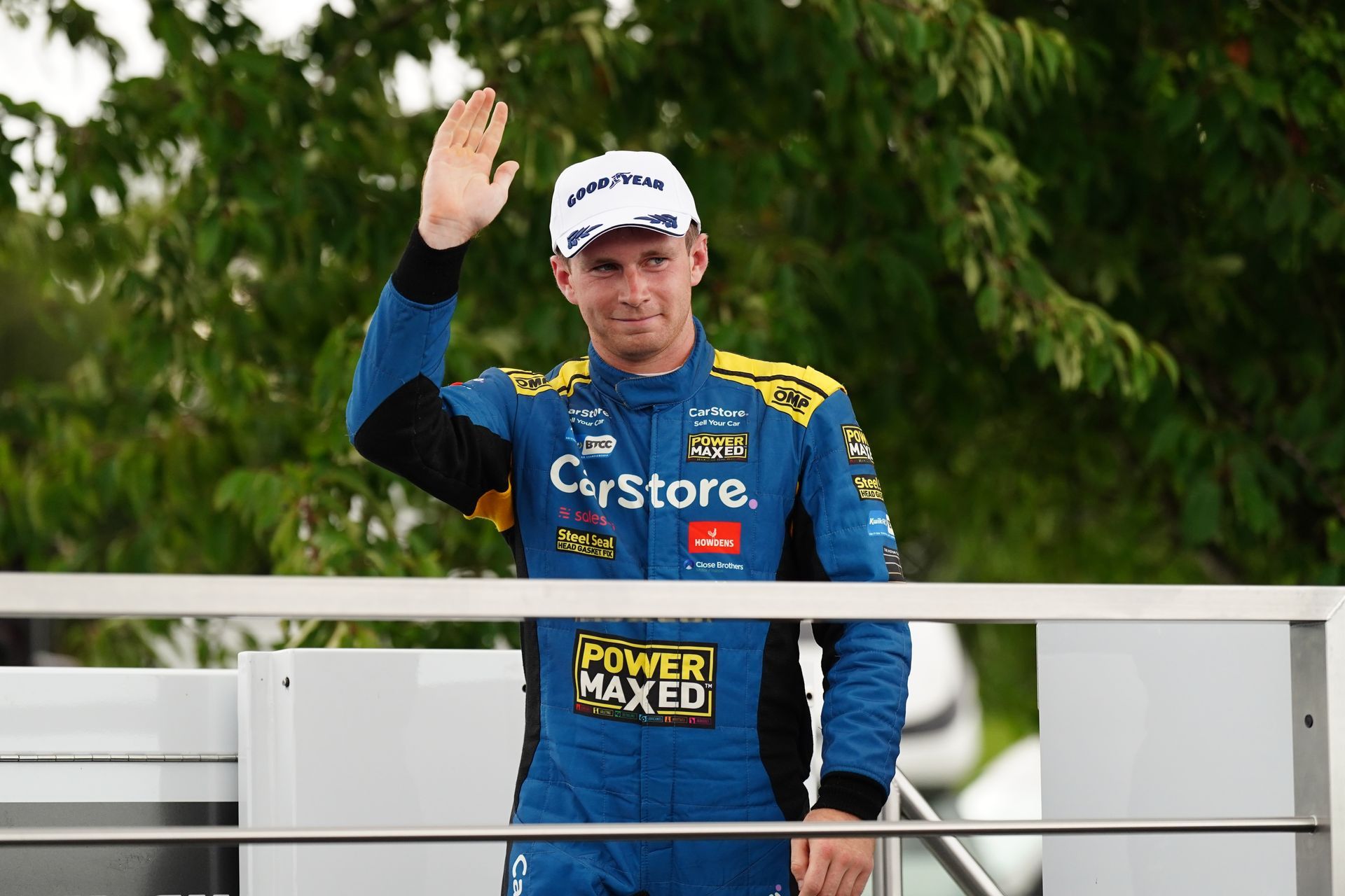 A man in a blue and yellow racing suit is waving his hand.