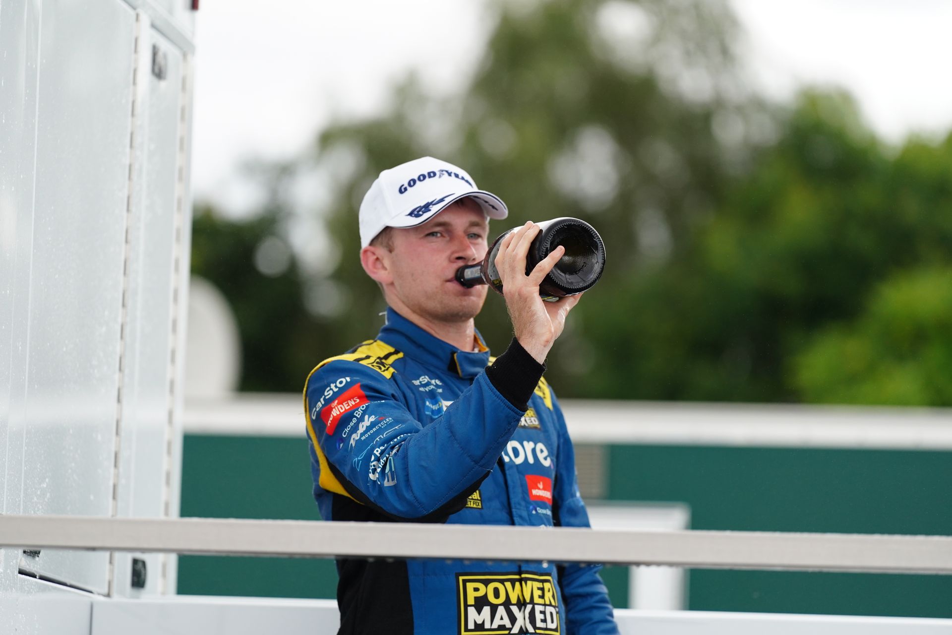 A man in a racing suit is drinking from a bottle.