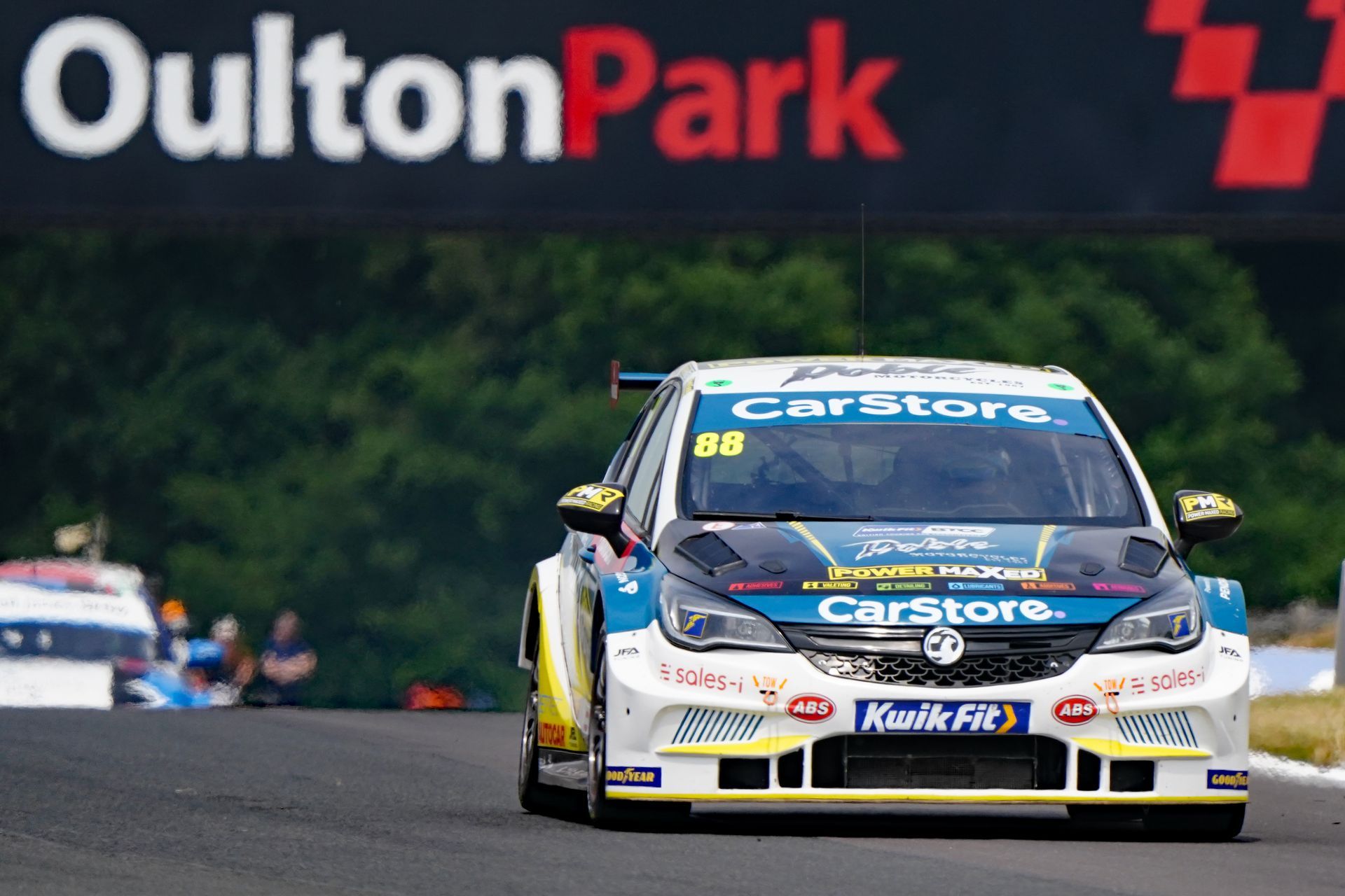 A race car is driving down a track in front of a sign that says oulton park