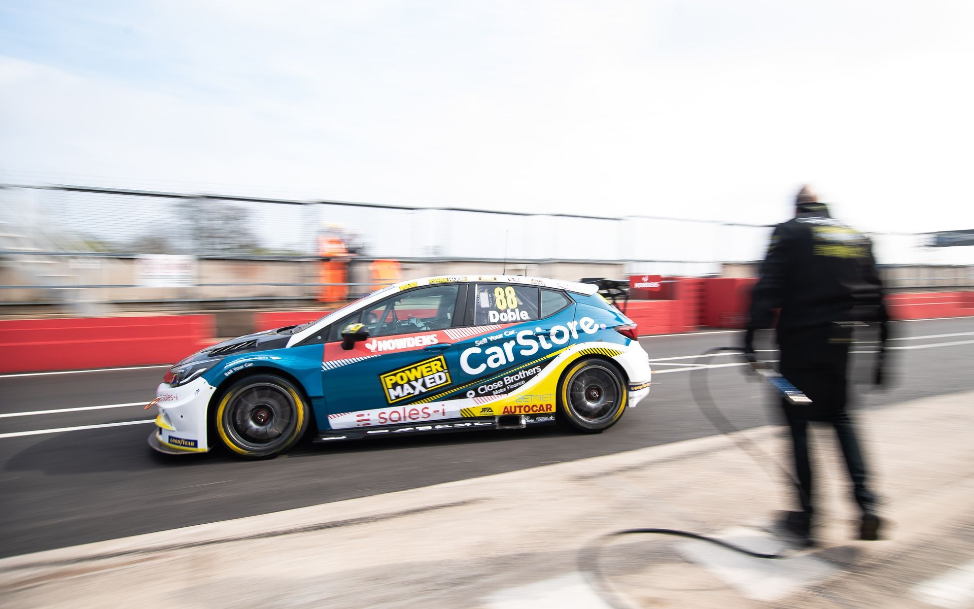 A race car is driving down a race track with a man walking behind it.