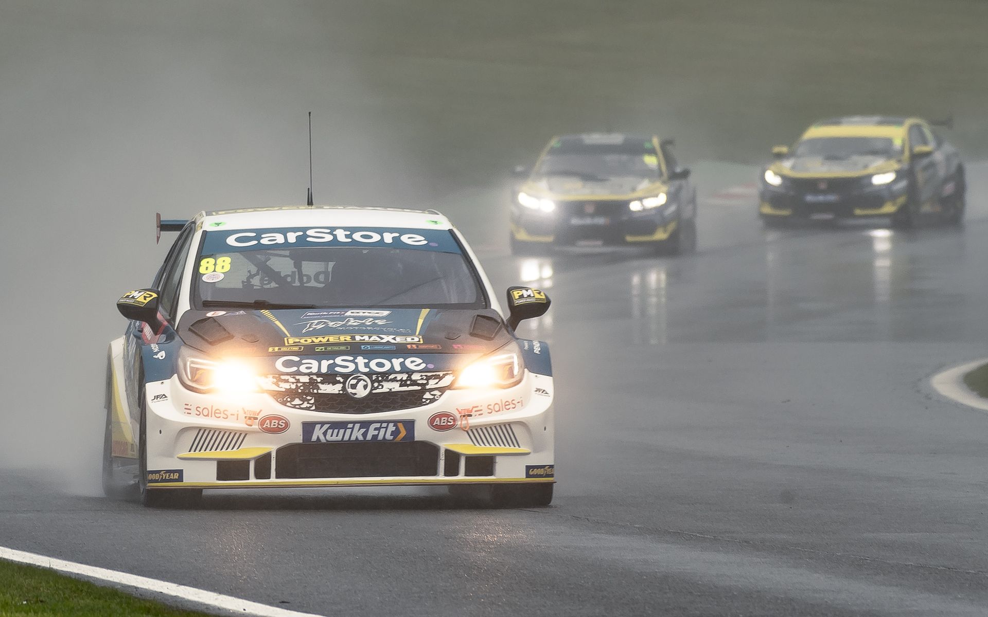 A race car is driving down a wet track in the rain.