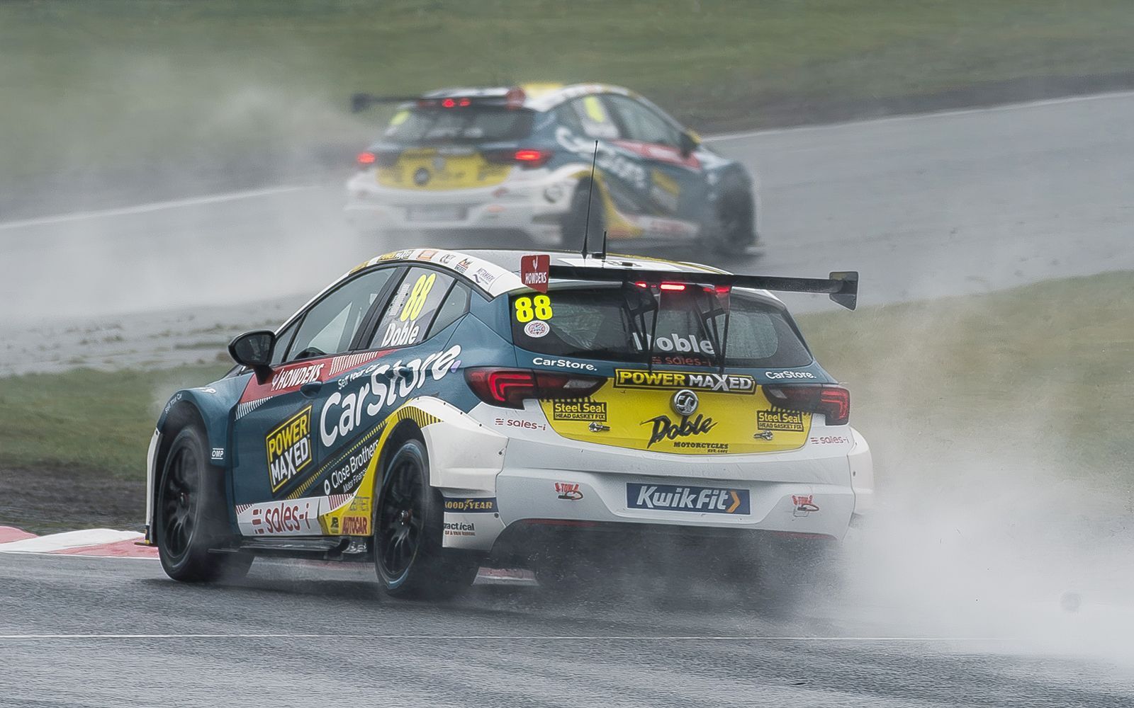 A group of racing cars are racing on a wet track.