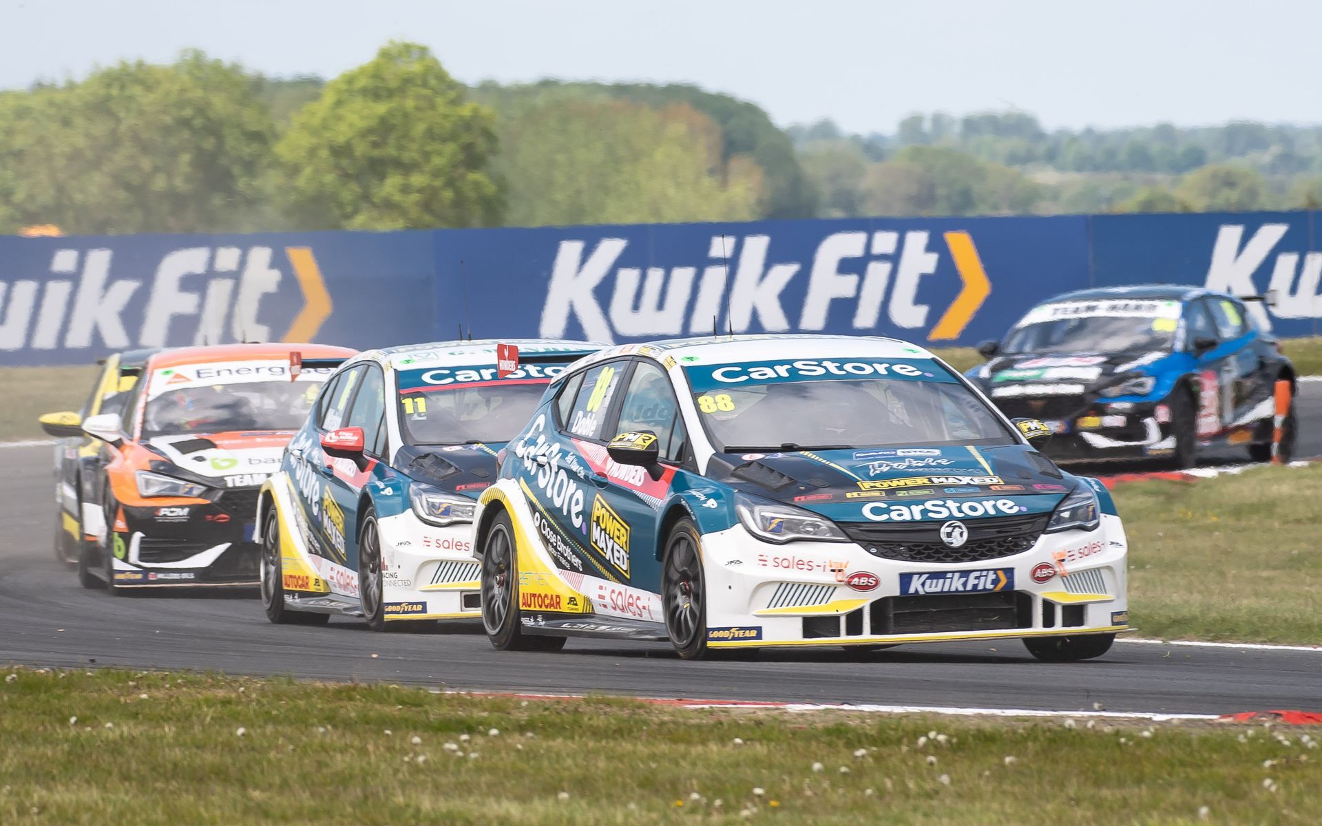 A group of race cars are racing on a track sponsored by kwik fit