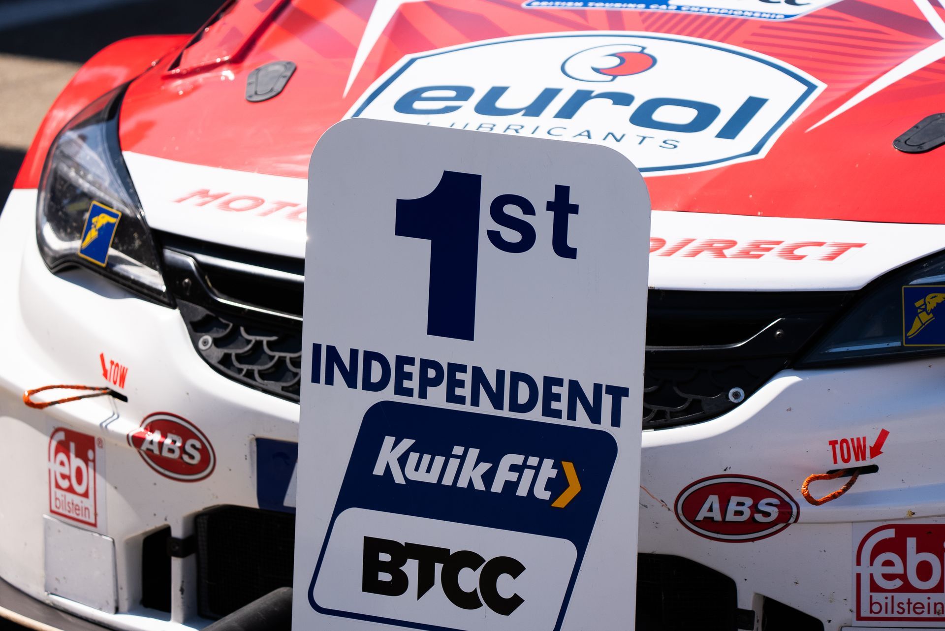 A red and white race car with a 1st independent kwikfit sign in front of it