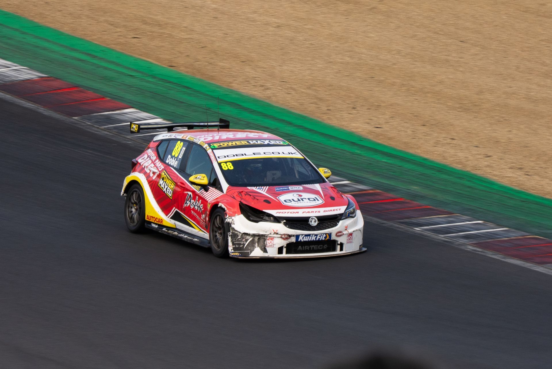 A red and yellow race car is driving down a race track.