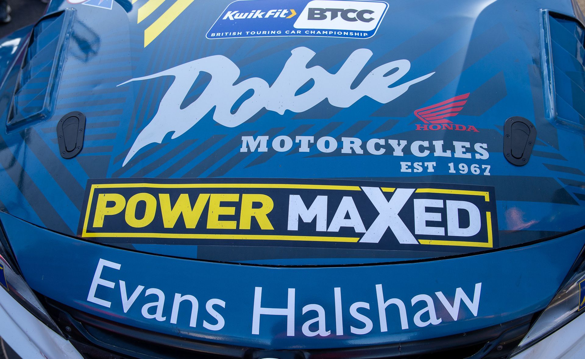 A blue motorcycle has a power maxed sticker on the hood