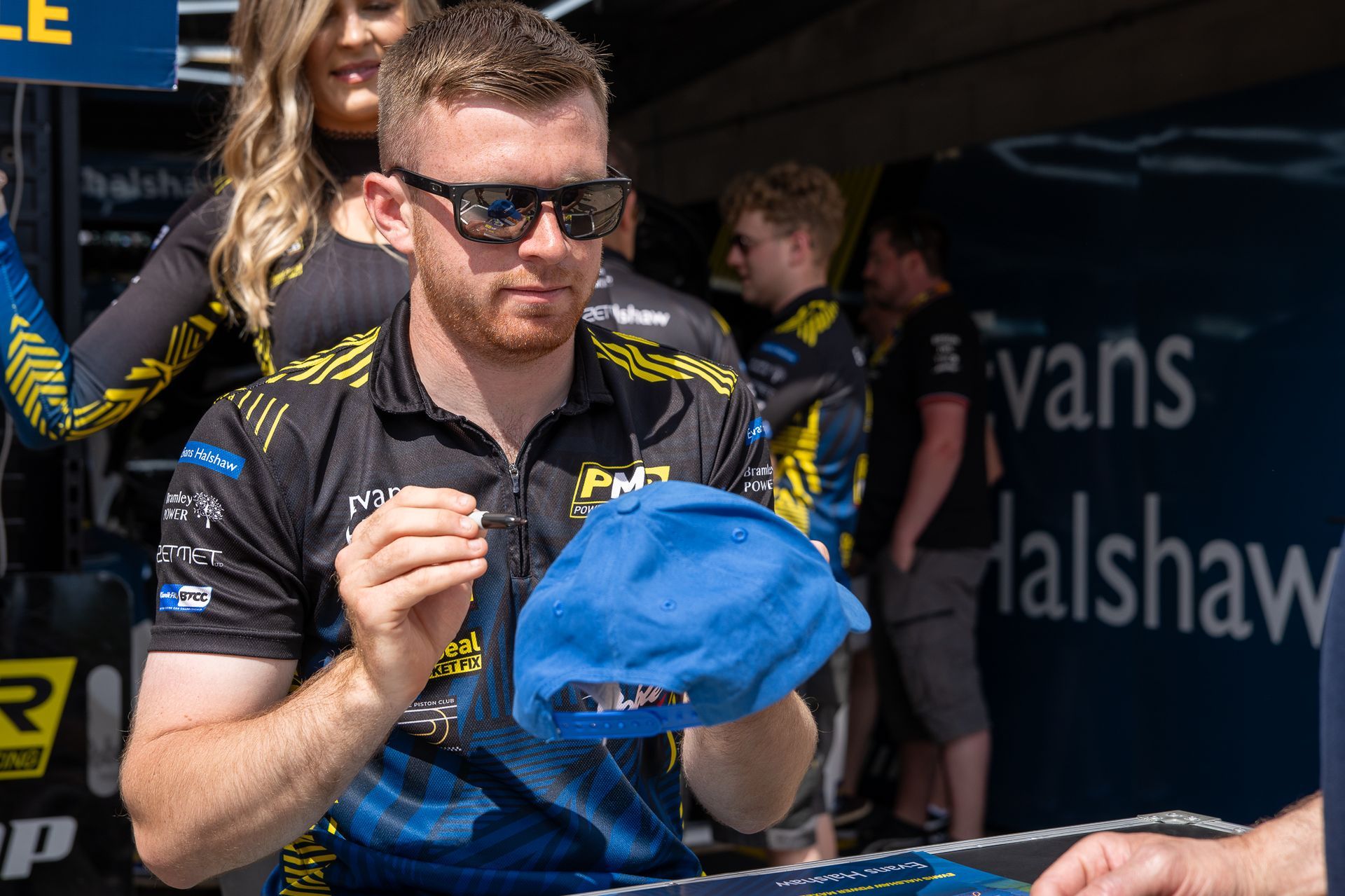 A man wearing sunglasses is holding a blue hat.