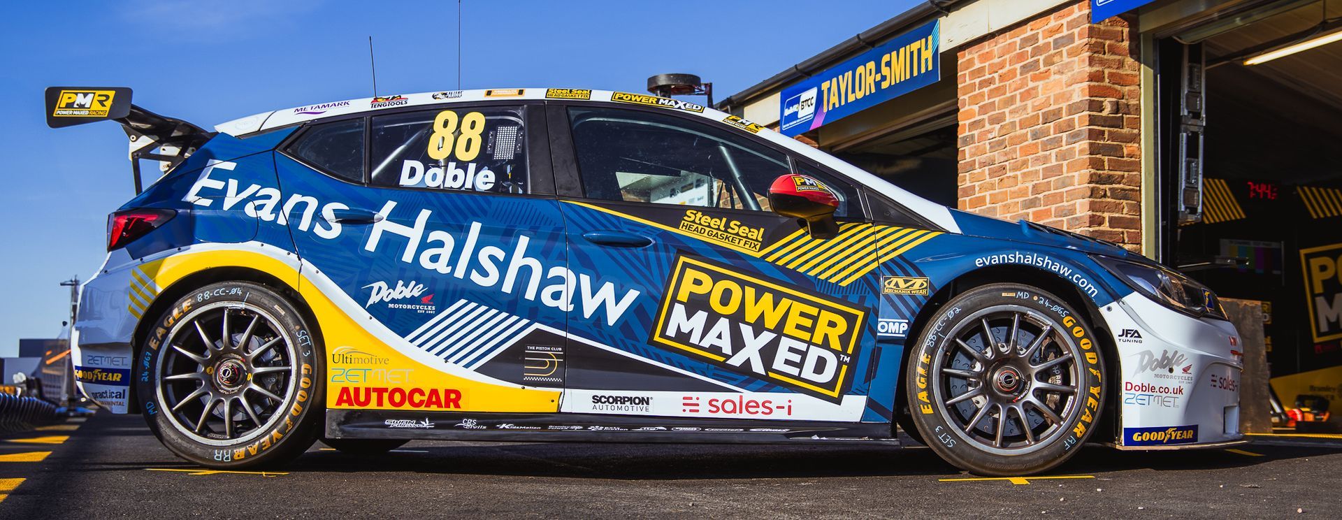 A blue and yellow race car is parked in front of a garage.