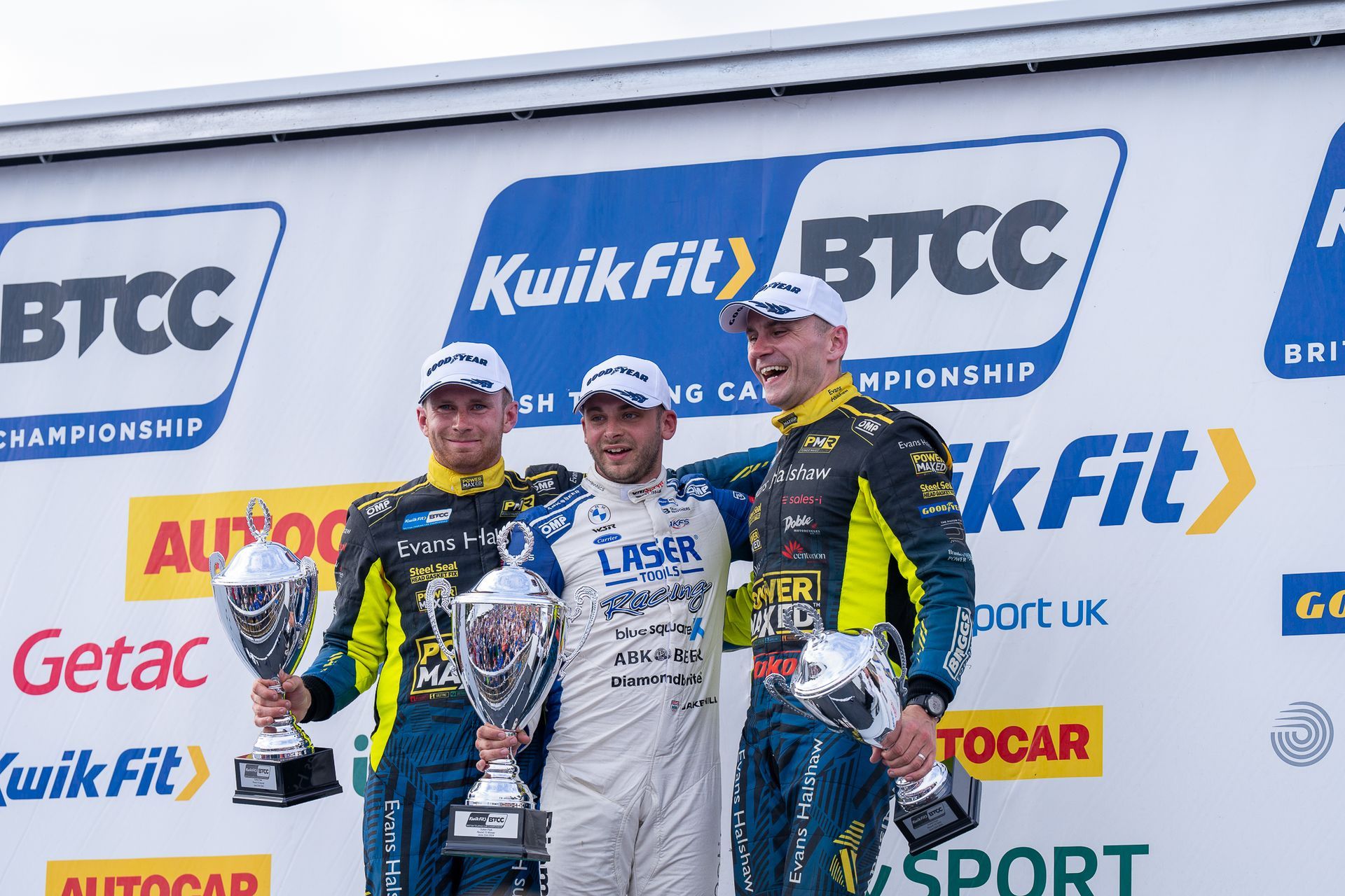 Three men holding trophies in front of a sign that says kwik fit