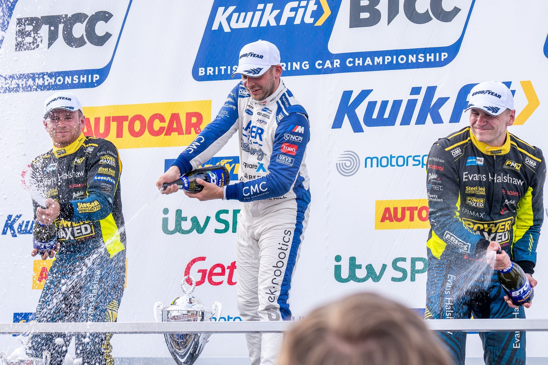A group of men are standing on a podium in front of a wall that says kwikfit