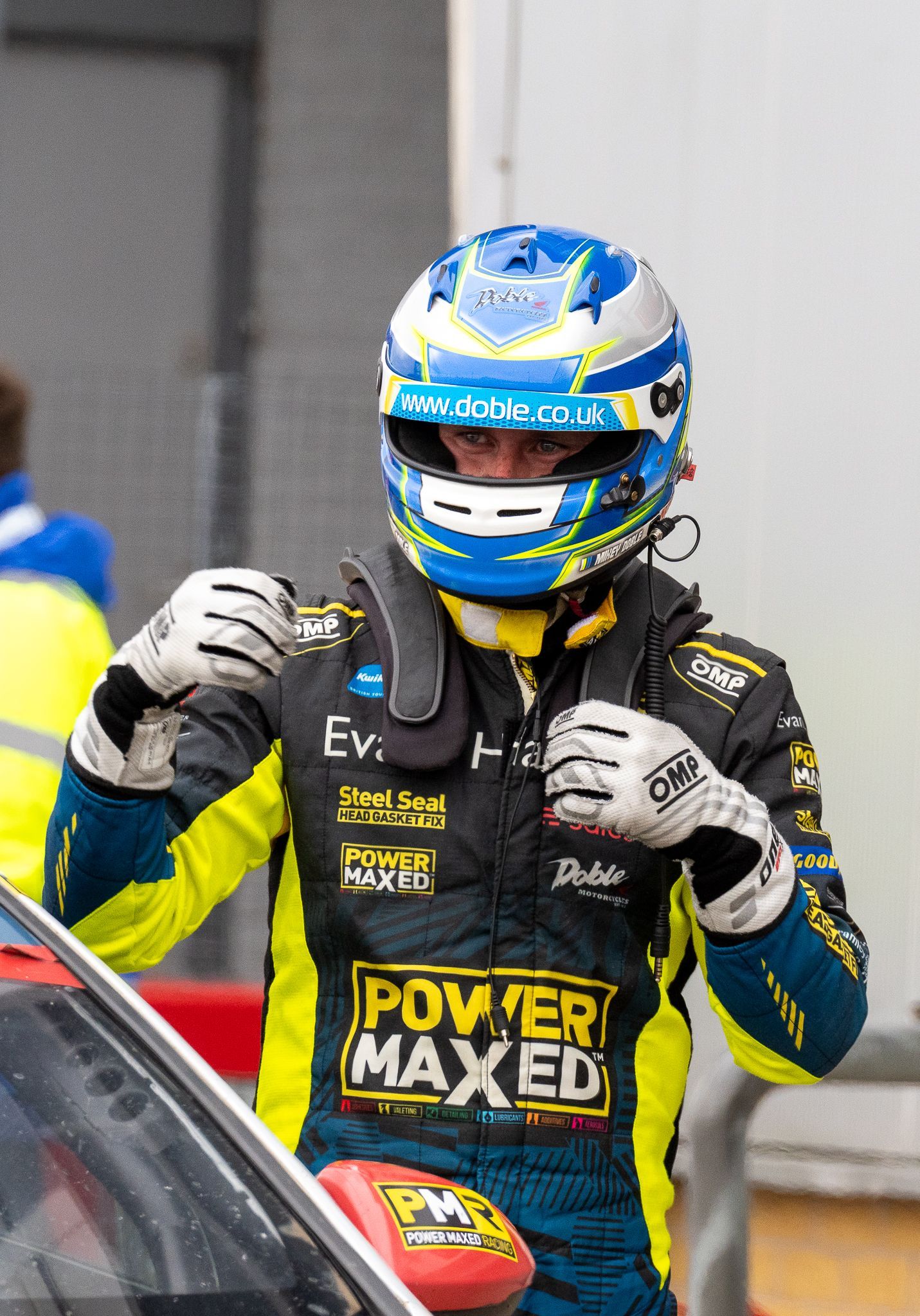 A man wearing a helmet and gloves is standing next to a car.