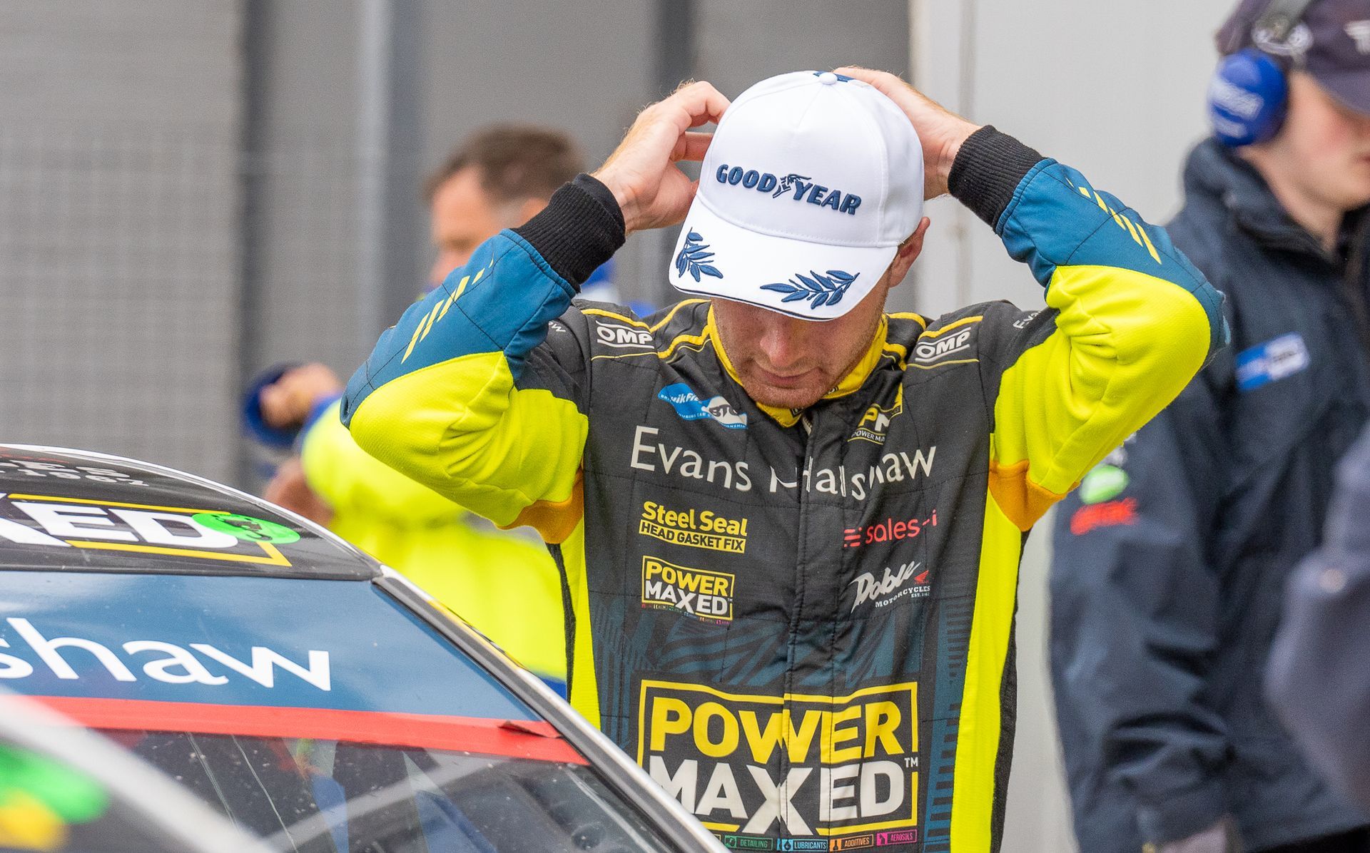 A man wearing a hat is standing in front of a race car.