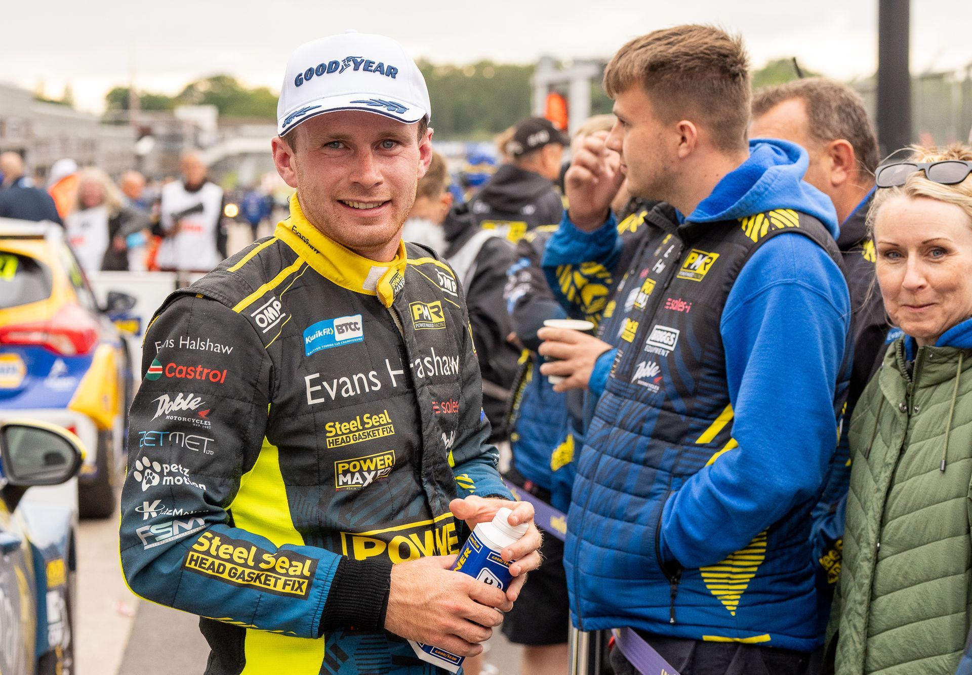 A man in a racing suit is standing next to a group of people.