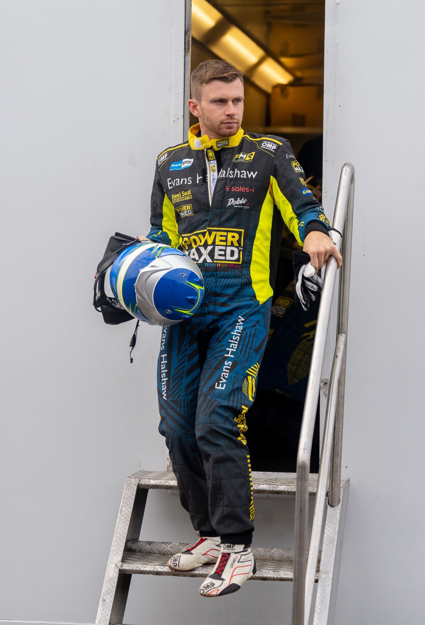 A man in a racing suit is standing on a set of stairs holding a helmet.