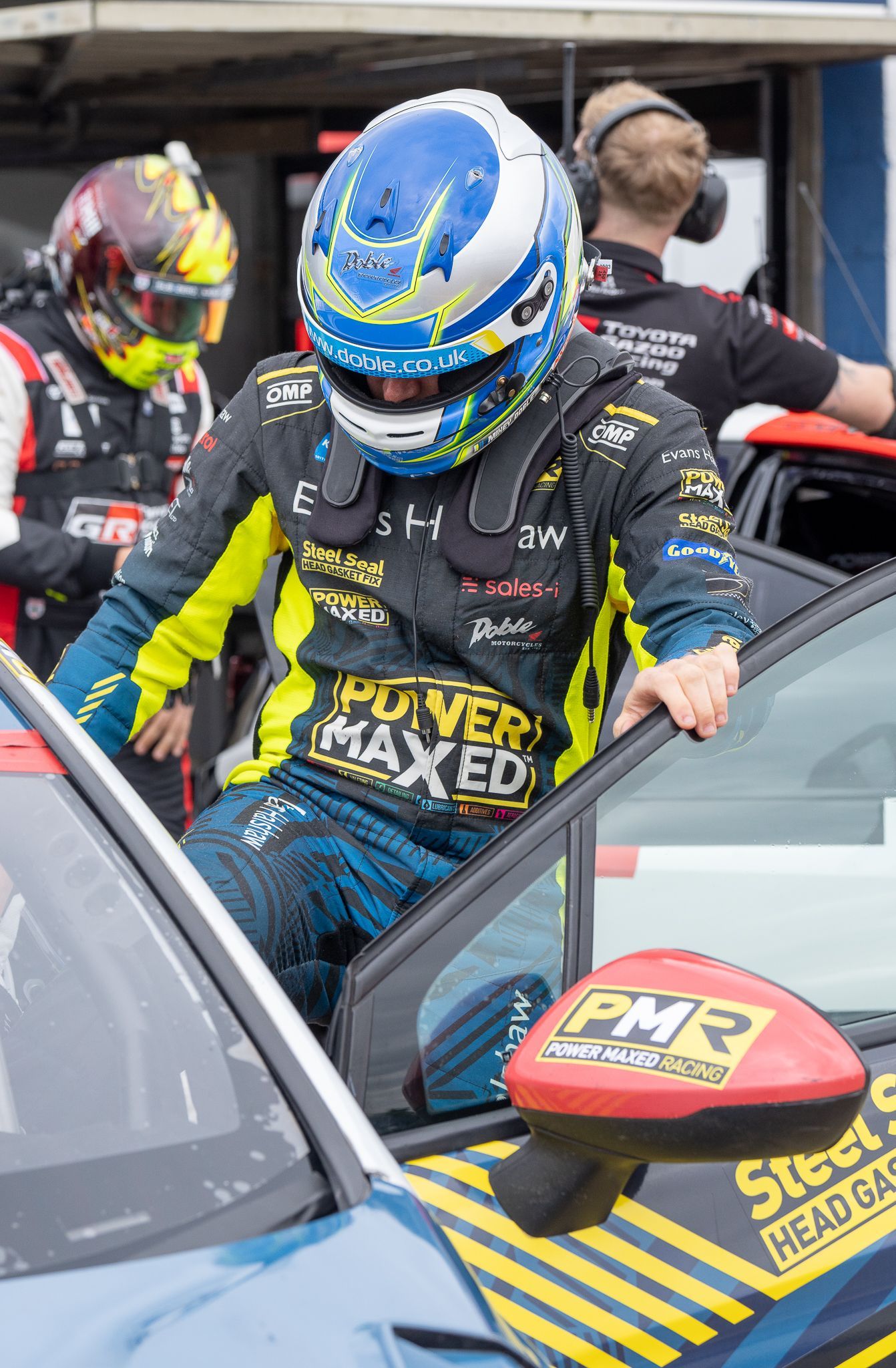 A man wearing a helmet is getting out of a race car.