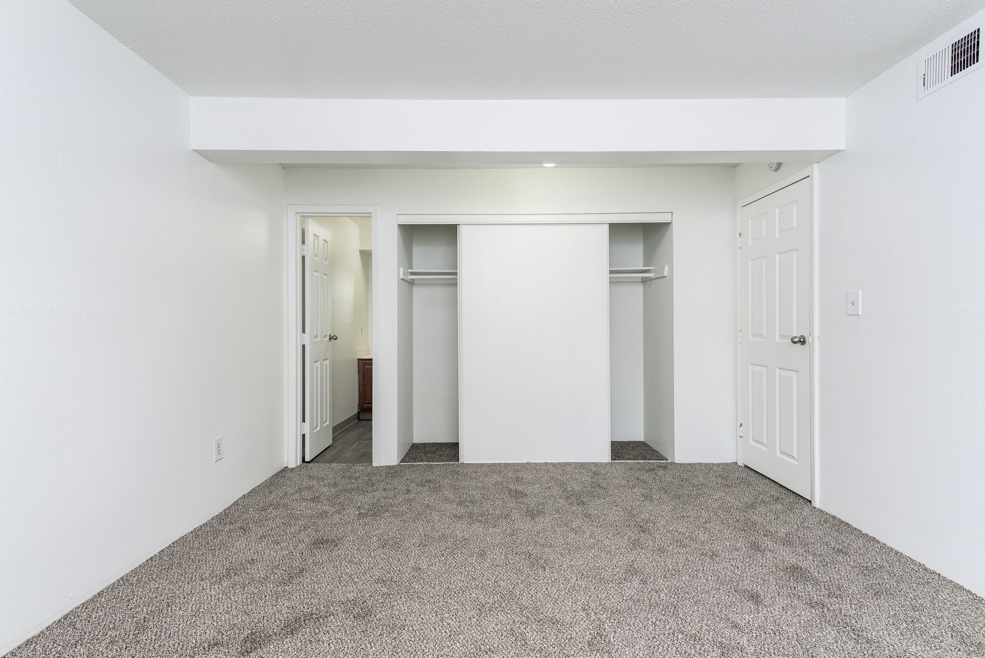 An empty bedroom with two closets and a carpeted floor.