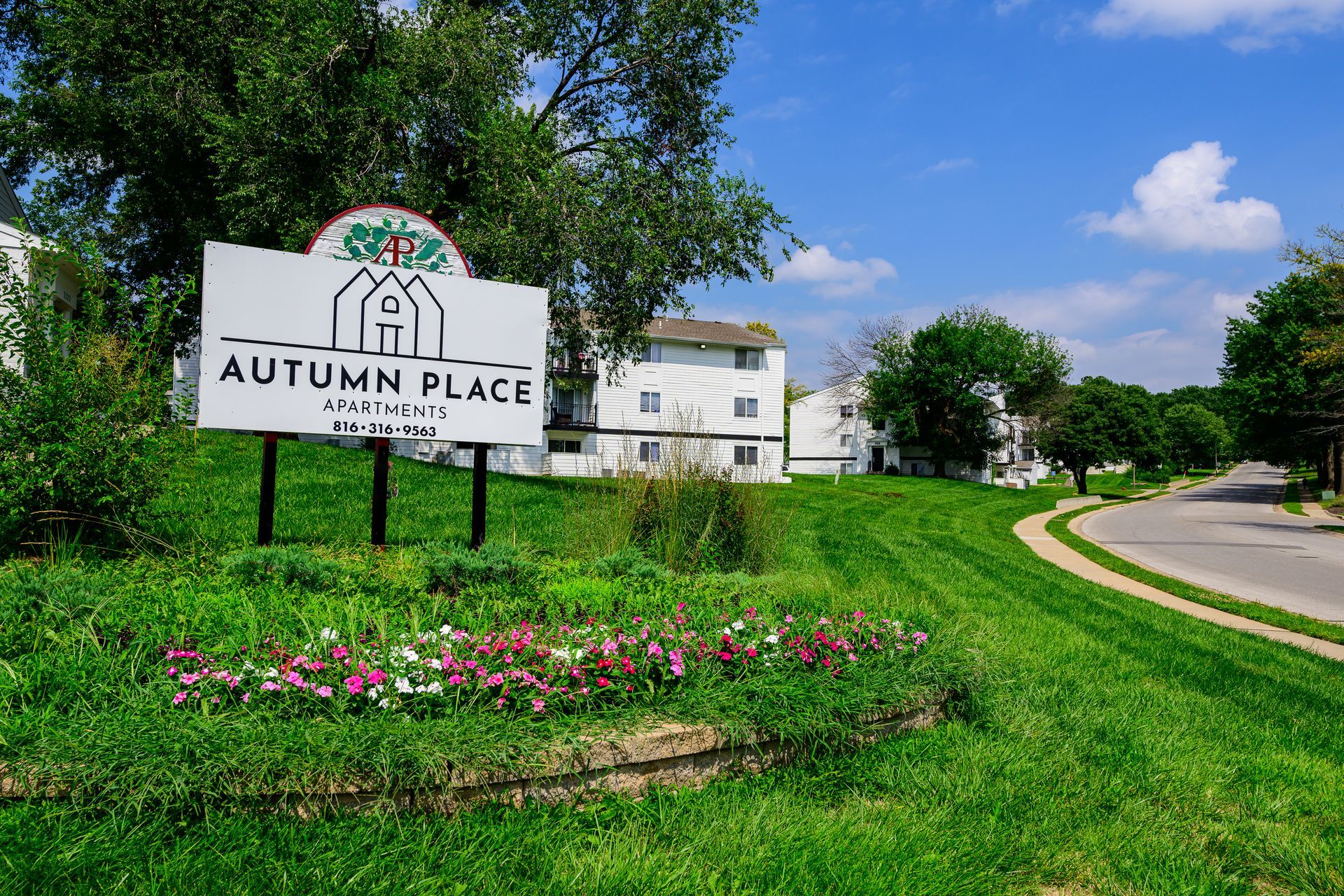 A sign for autumn place is sitting in the middle of a lush green field.