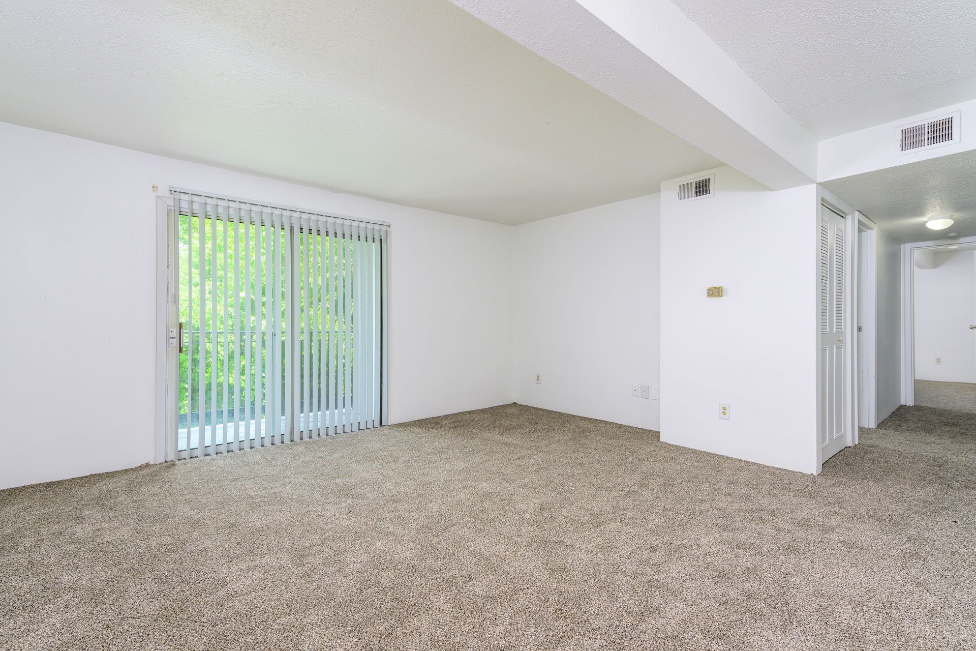 An empty living room with a sliding glass door and a balcony.