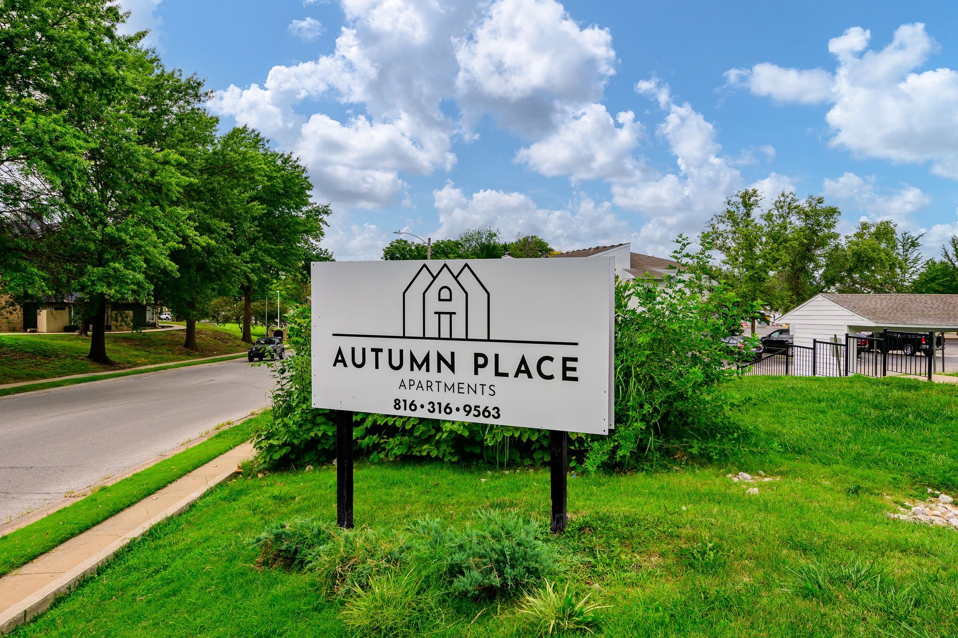 A sign for autumn place is sitting in the middle of a lush green field.