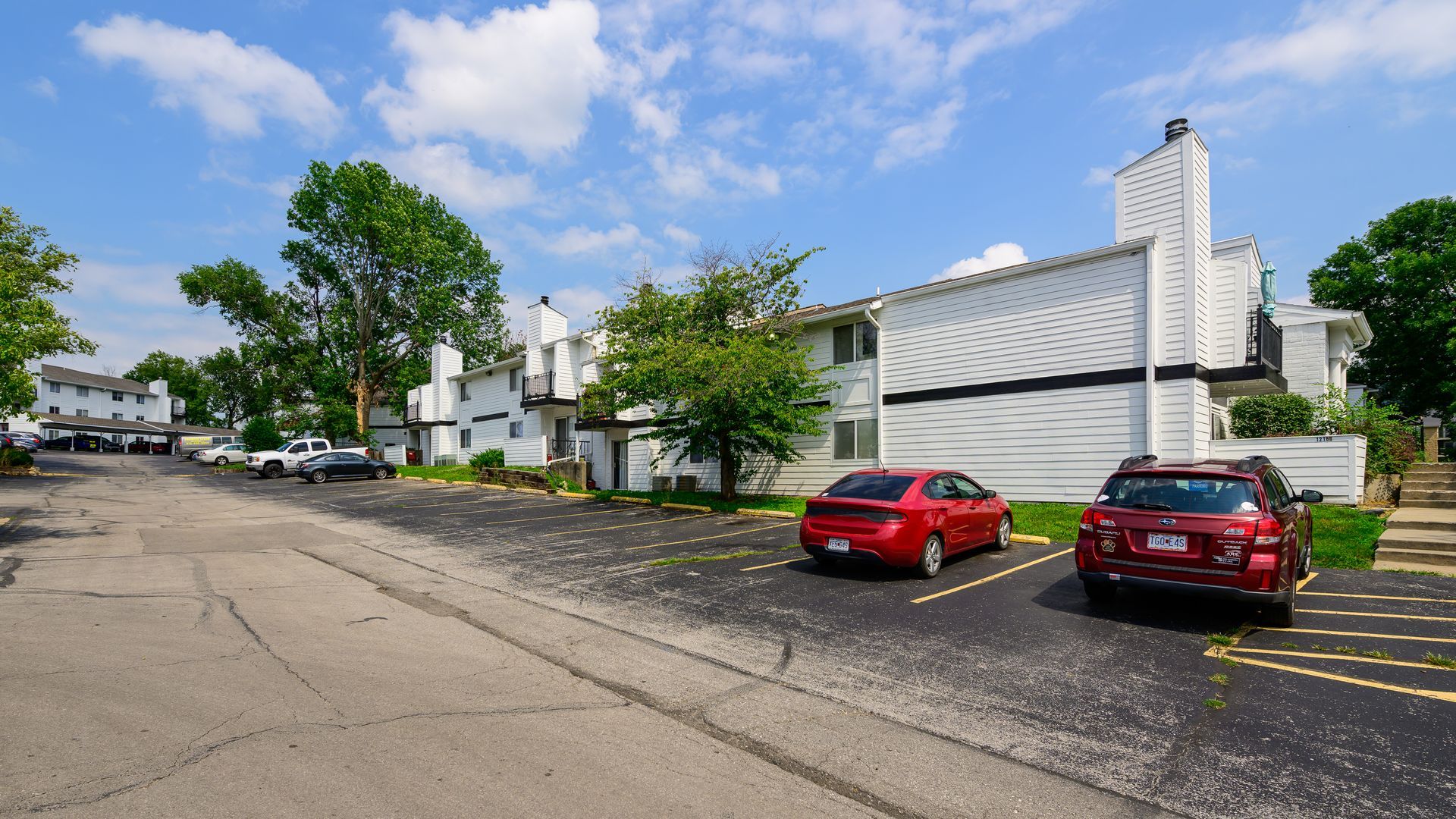 A row of cars are parked in a parking lot in front of a building.