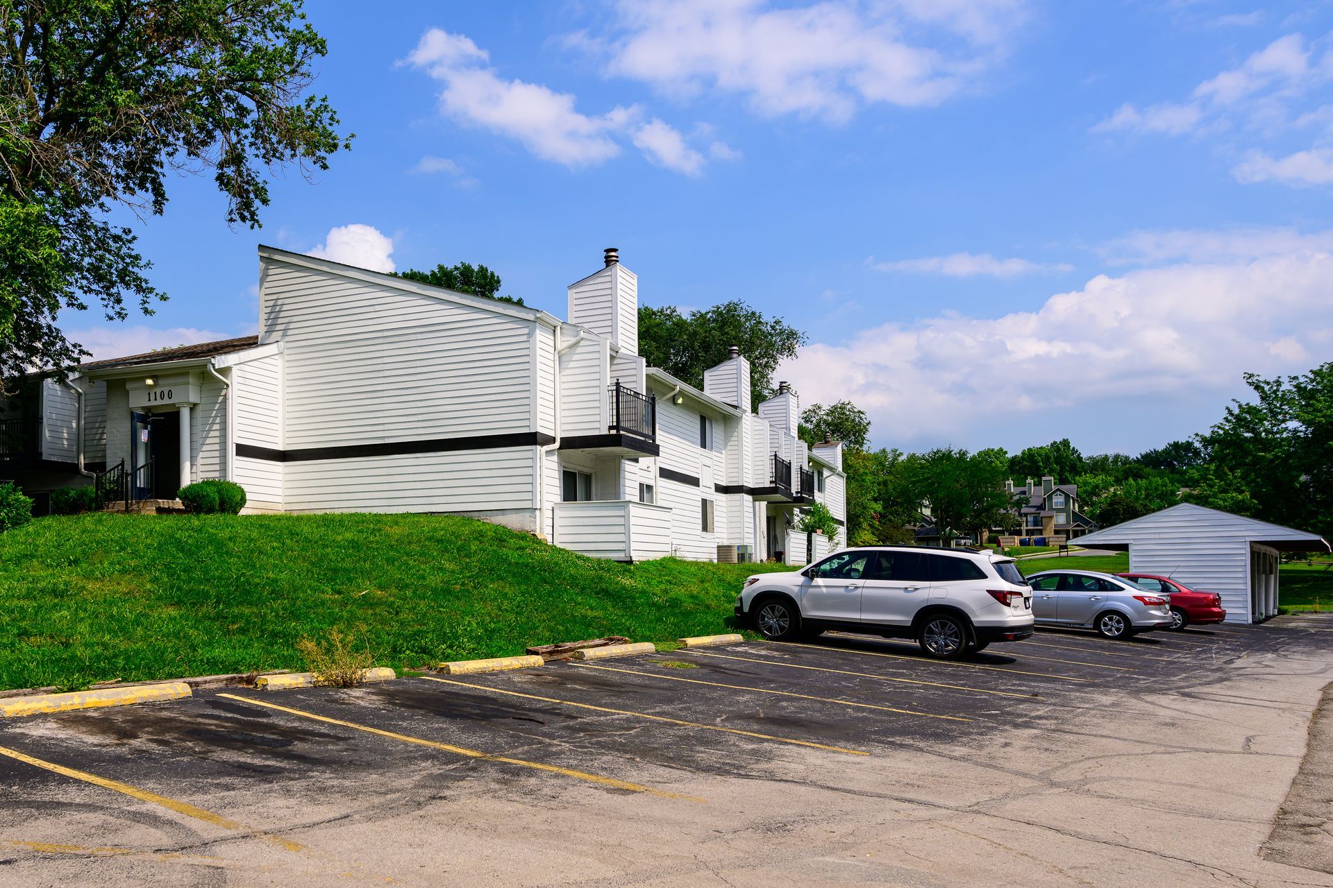 A row of cars are parked in front of a white apartment building.
