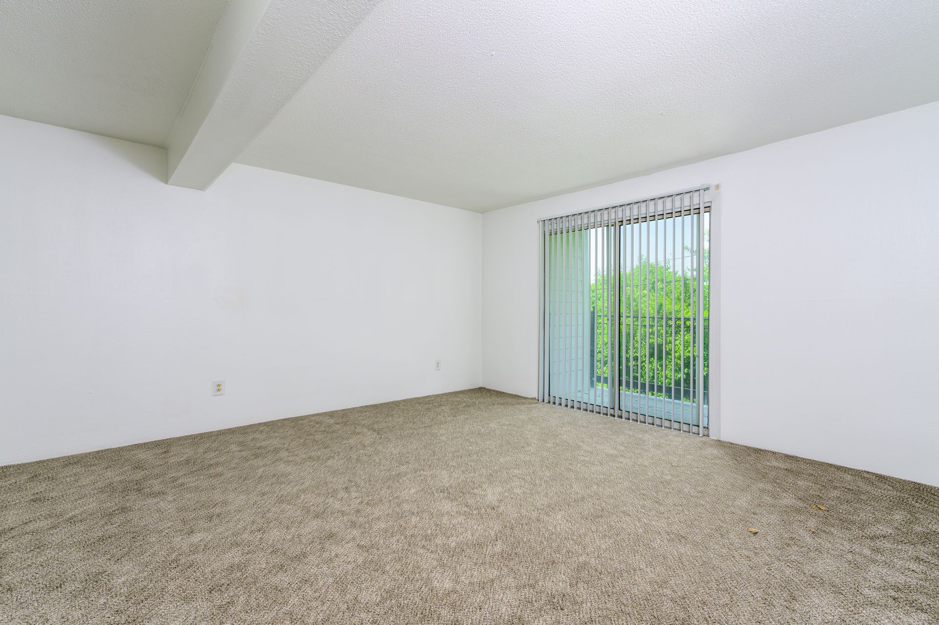 An empty living room with a sliding glass door and a balcony.