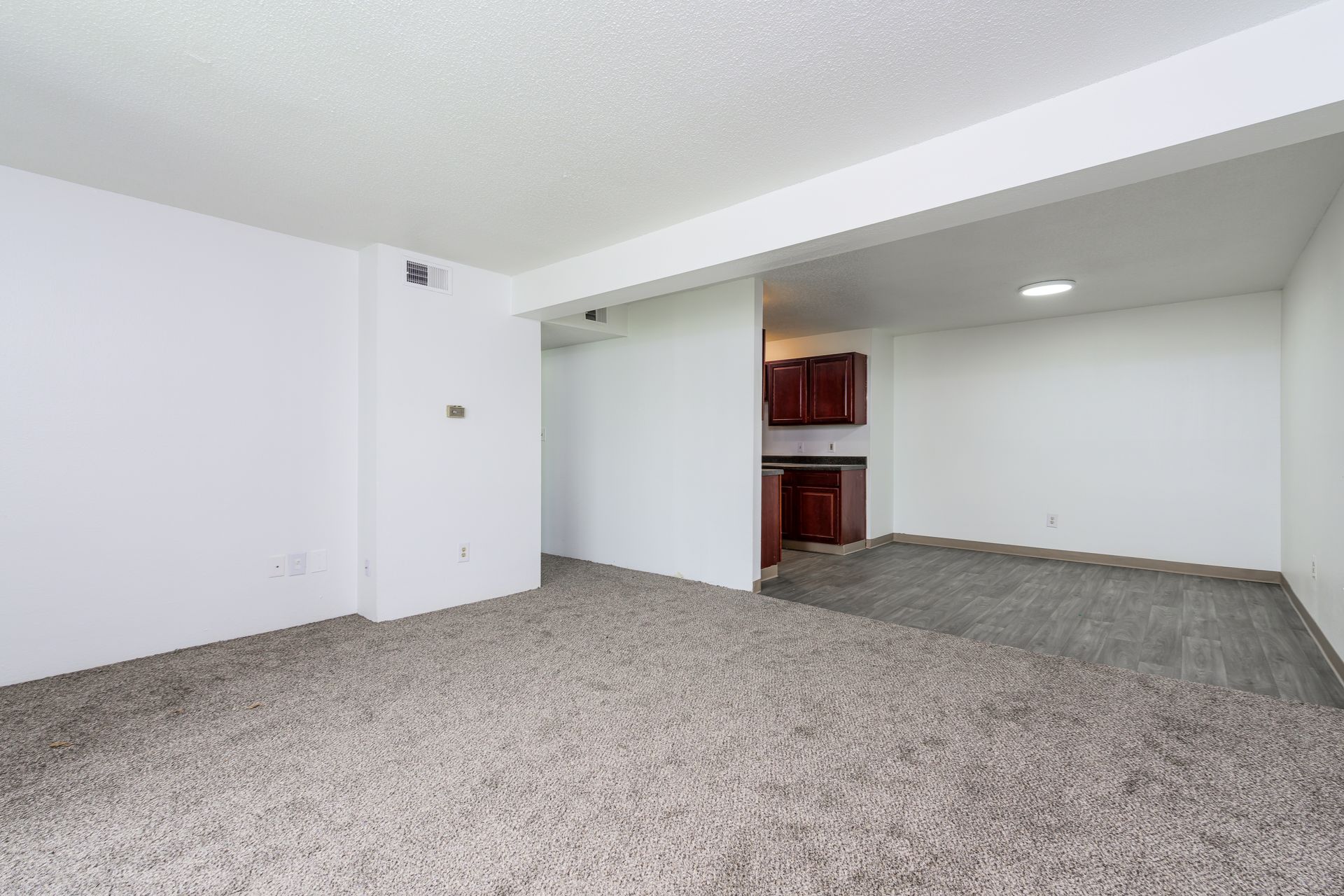 An empty living room with a carpeted floor and white walls.
