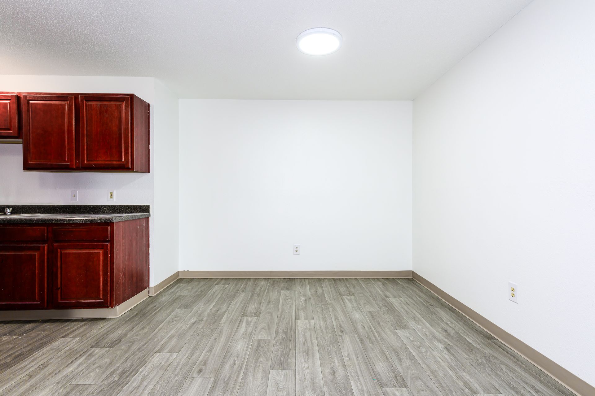 An empty room with a kitchen and wooden floors.