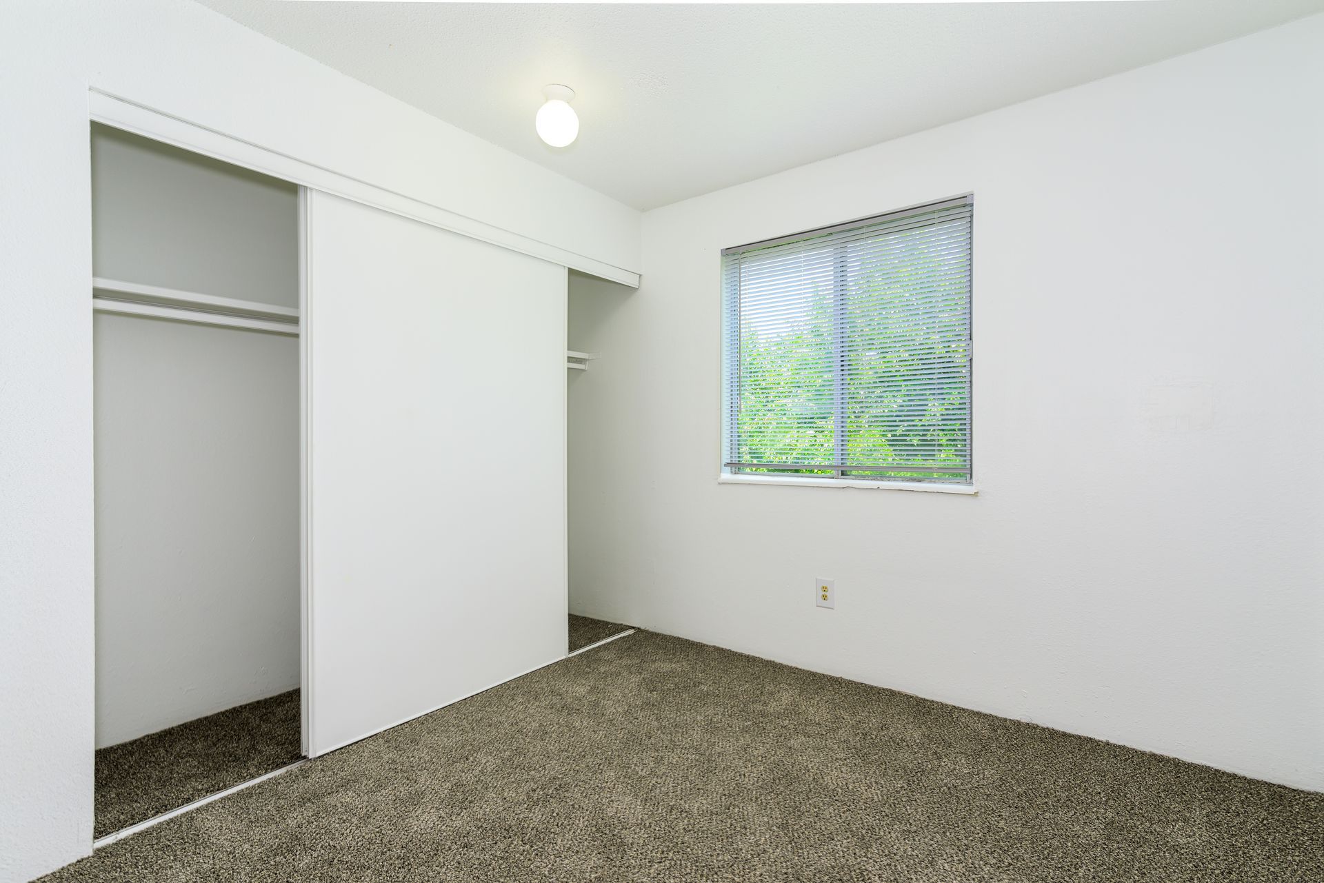 An empty bedroom with a closet and a window.