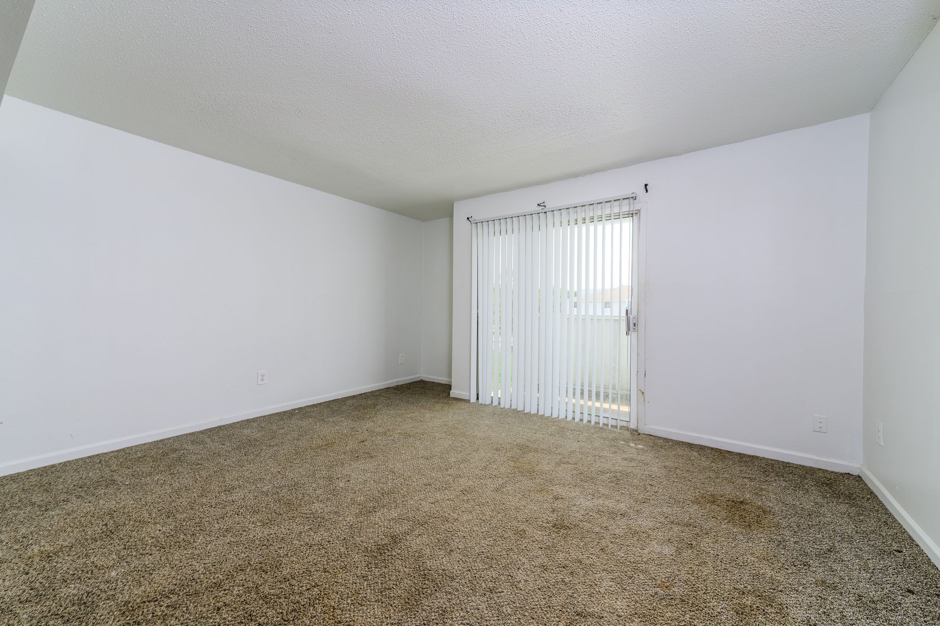 An empty living room with a sliding glass door and a balcony.