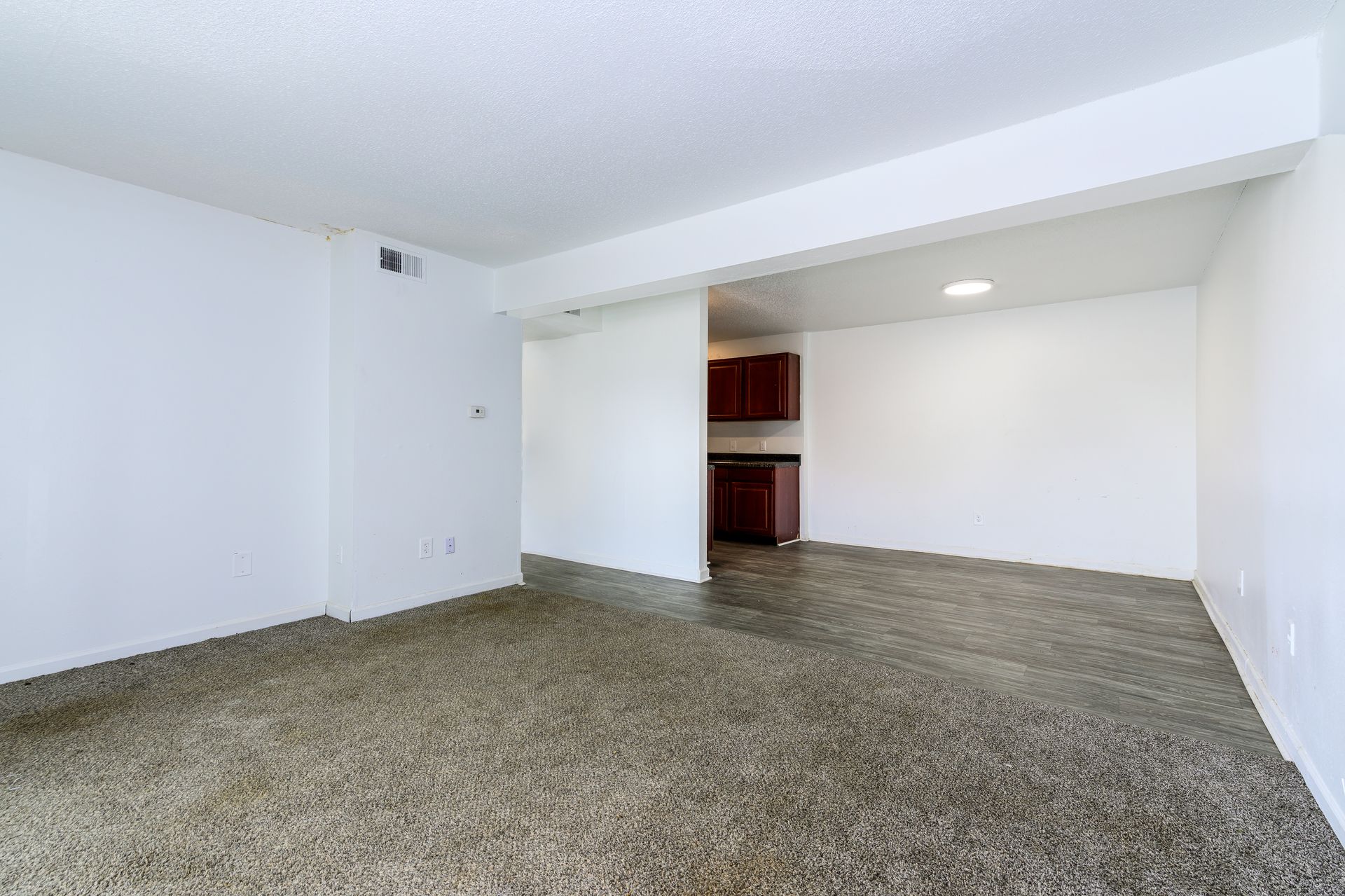 An empty living room with a carpeted floor and white walls.