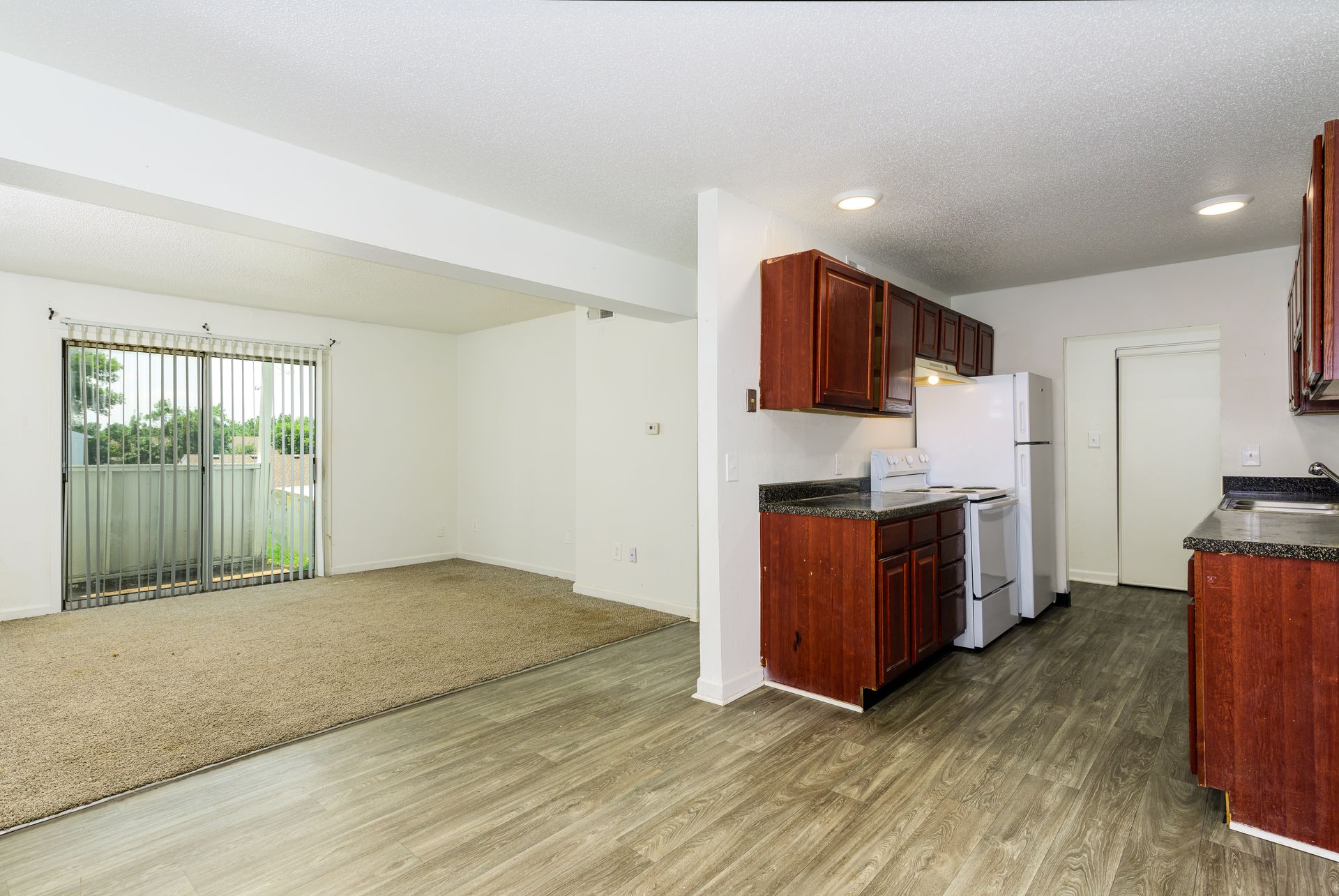 An empty apartment with a living room , kitchen and sliding glass doors.