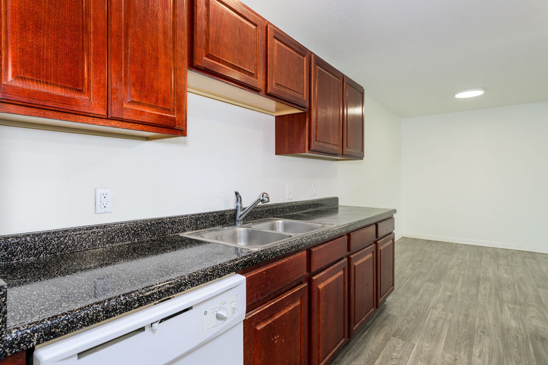 A kitchen with wooden cabinets , granite counter tops , a sink and a dishwasher.