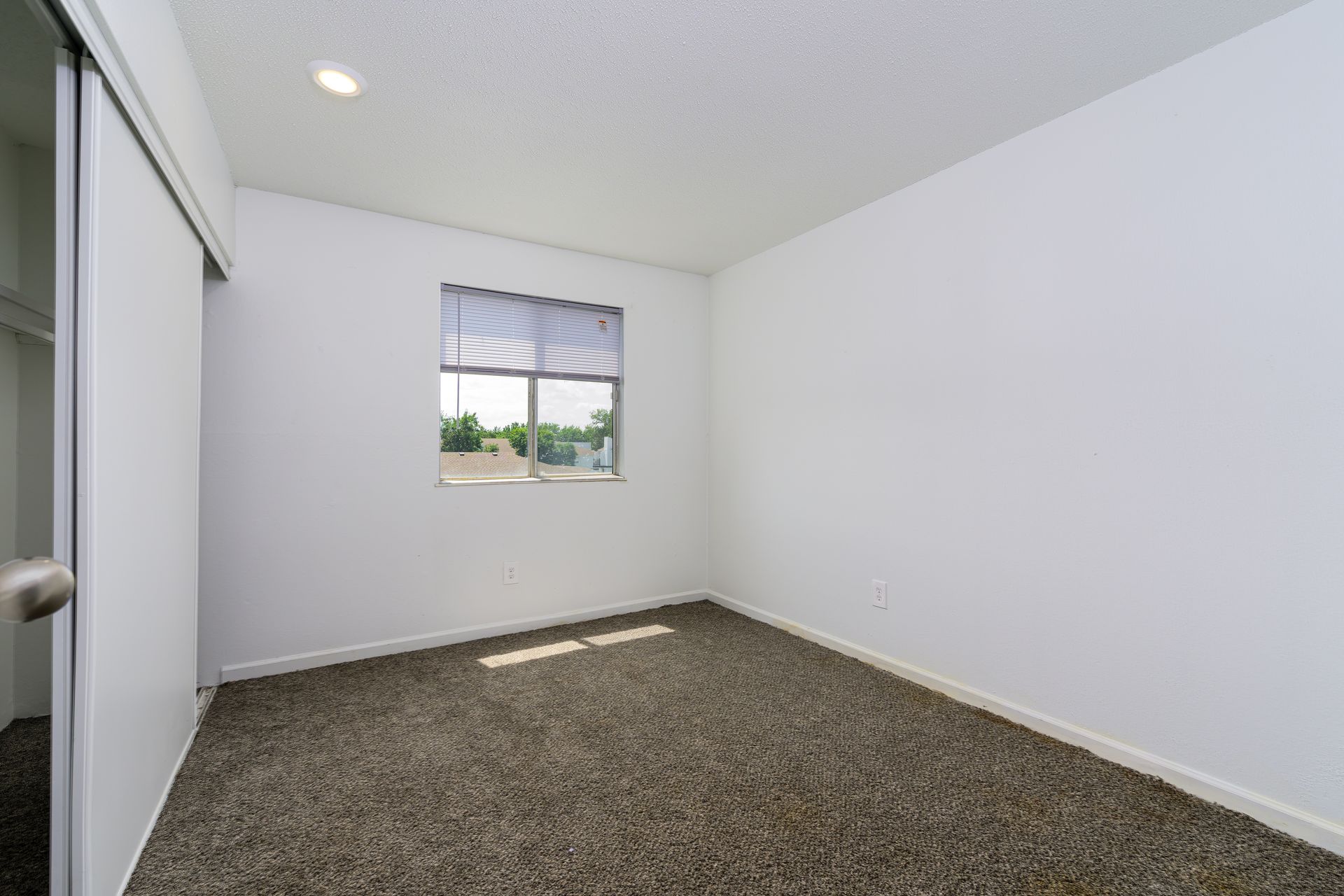 An empty bedroom with a window and carpet.
