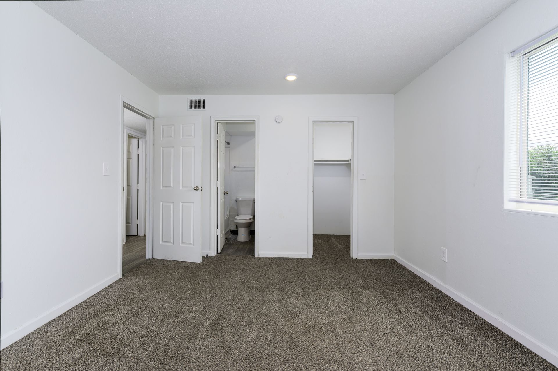 An empty bedroom with a toilet , closet and window.