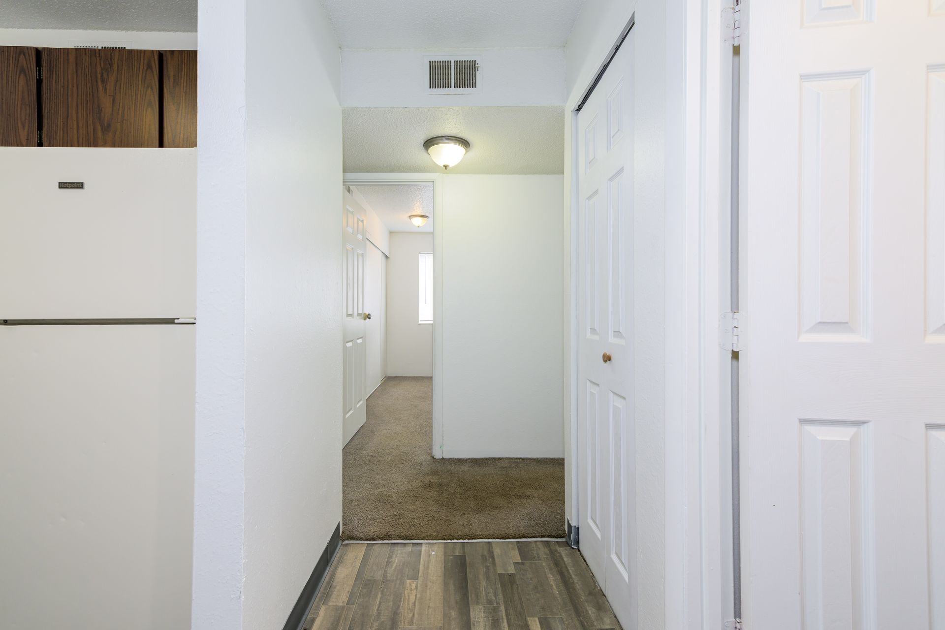 A hallway in a house with a refrigerator and a closet.