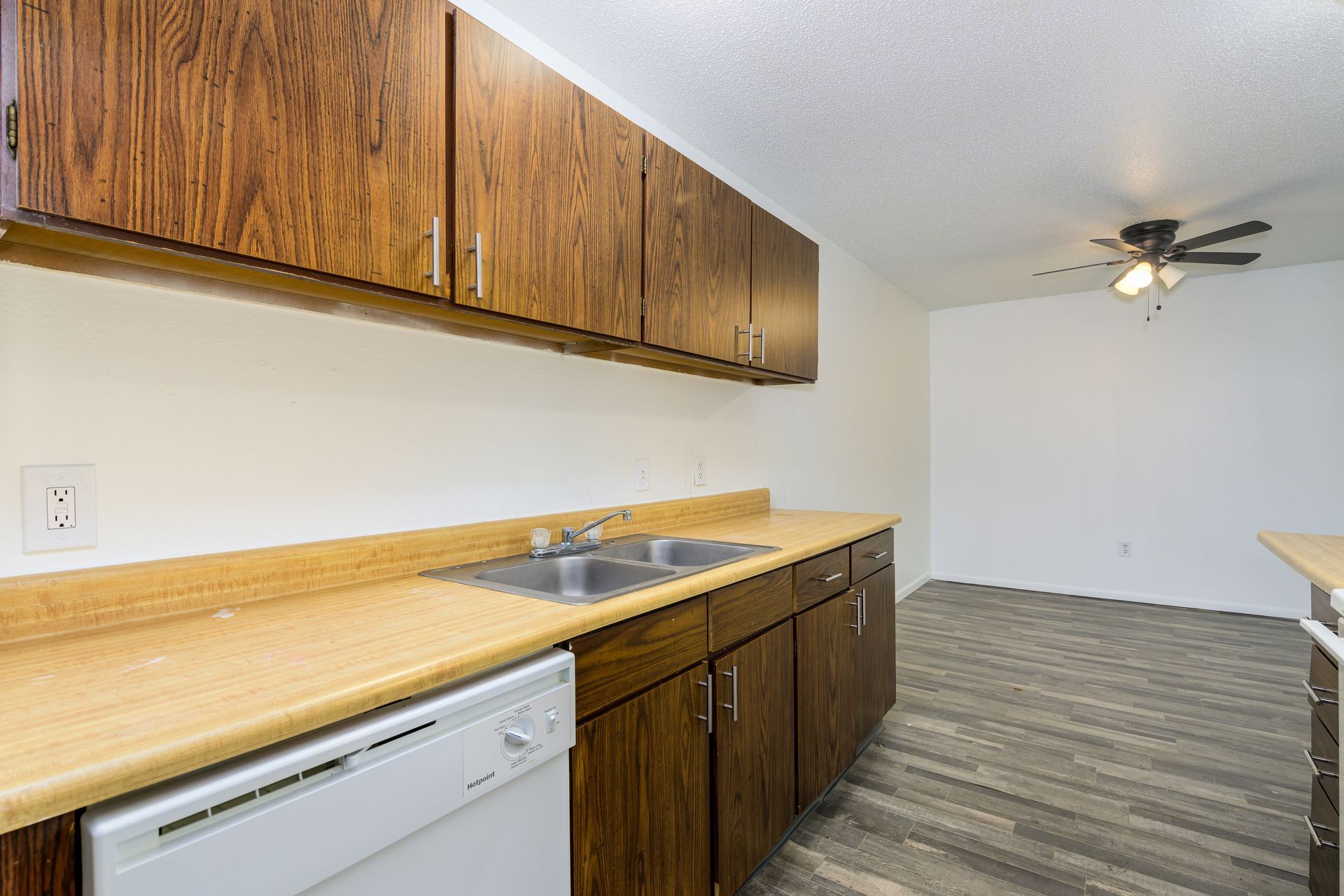 A kitchen with wooden cabinets , a sink , a dishwasher and a ceiling fan.